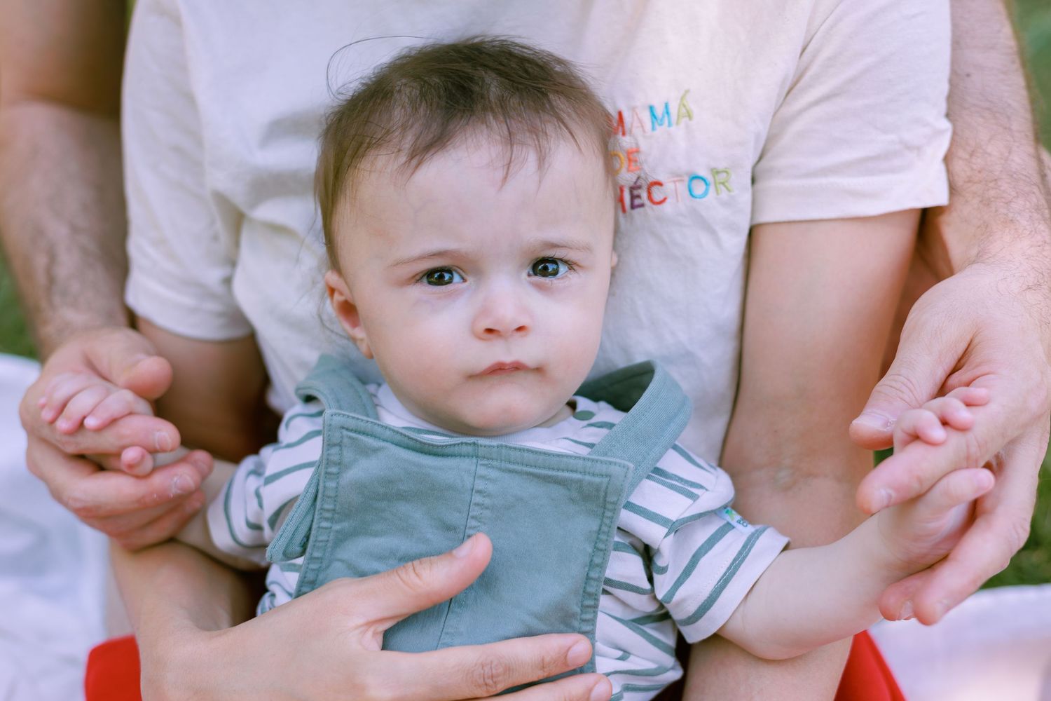 Un bébé regarde l’appareil photo dans les bras de ses parents pendant une séance photo famille.