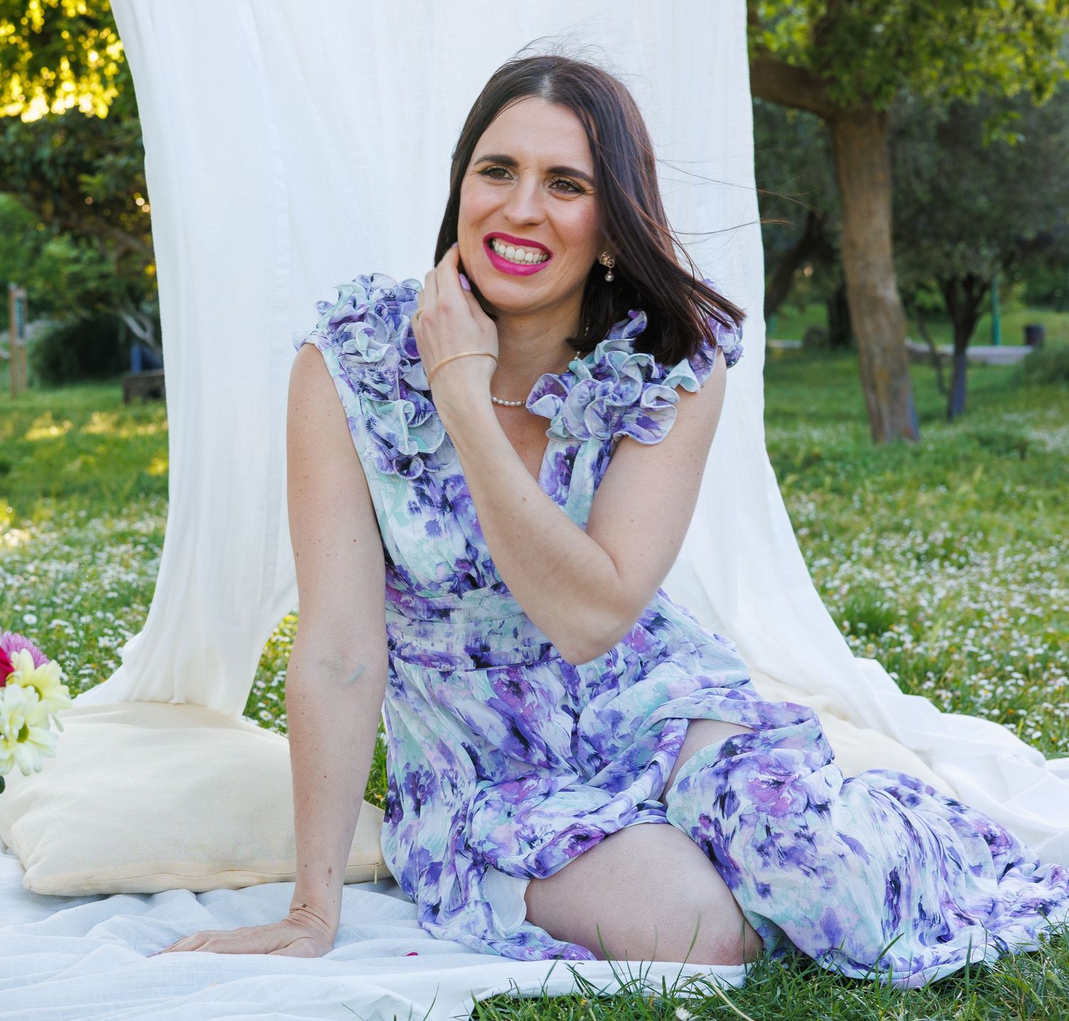 Une femme sourit assise dans un décor fleuri pendant une séance photo au parc
