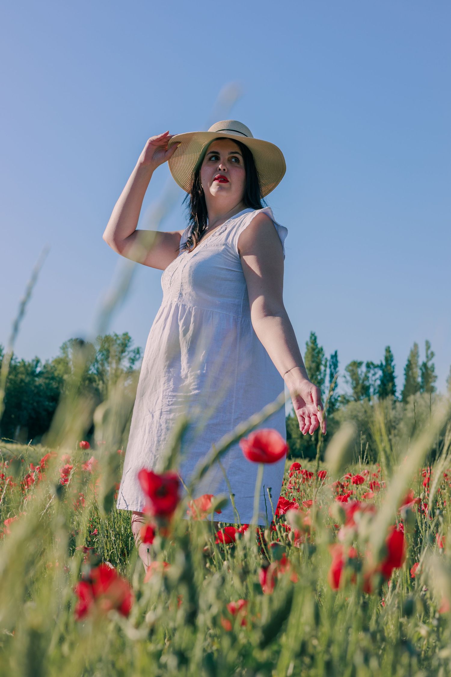 Une femme sourit au milieu d’un champ de coquelicots pendant une séance photo portrait.
