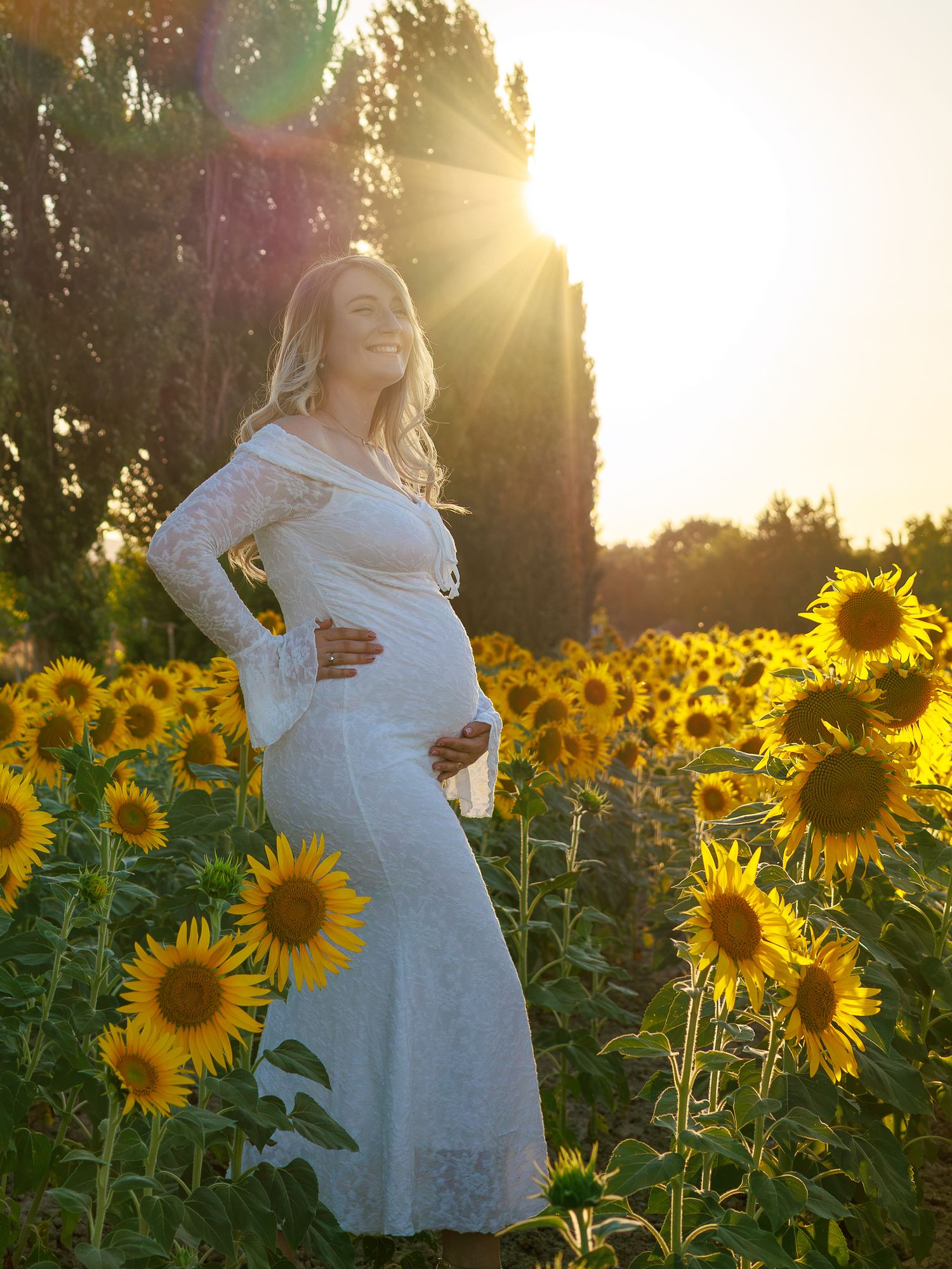 Une future maman pose dans un champ de tournesols au coucher du soleil pendant une séance photo grossesse en extérieur.