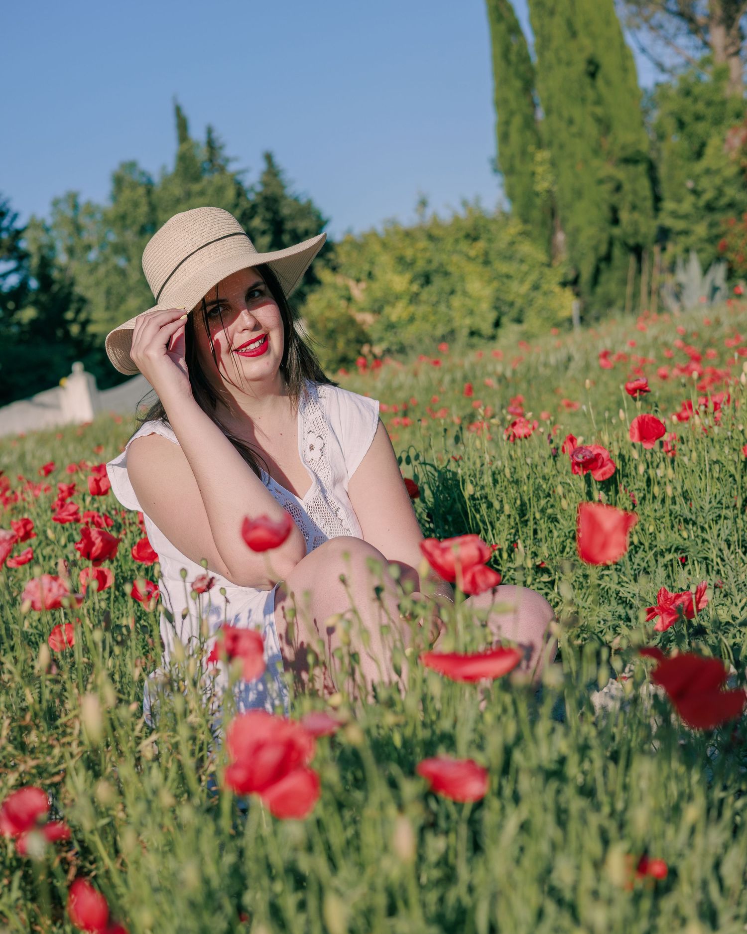 Une femme pose avec un chapeau dans un champ de coquelicots pendant une séance photo portrait en extérieur.