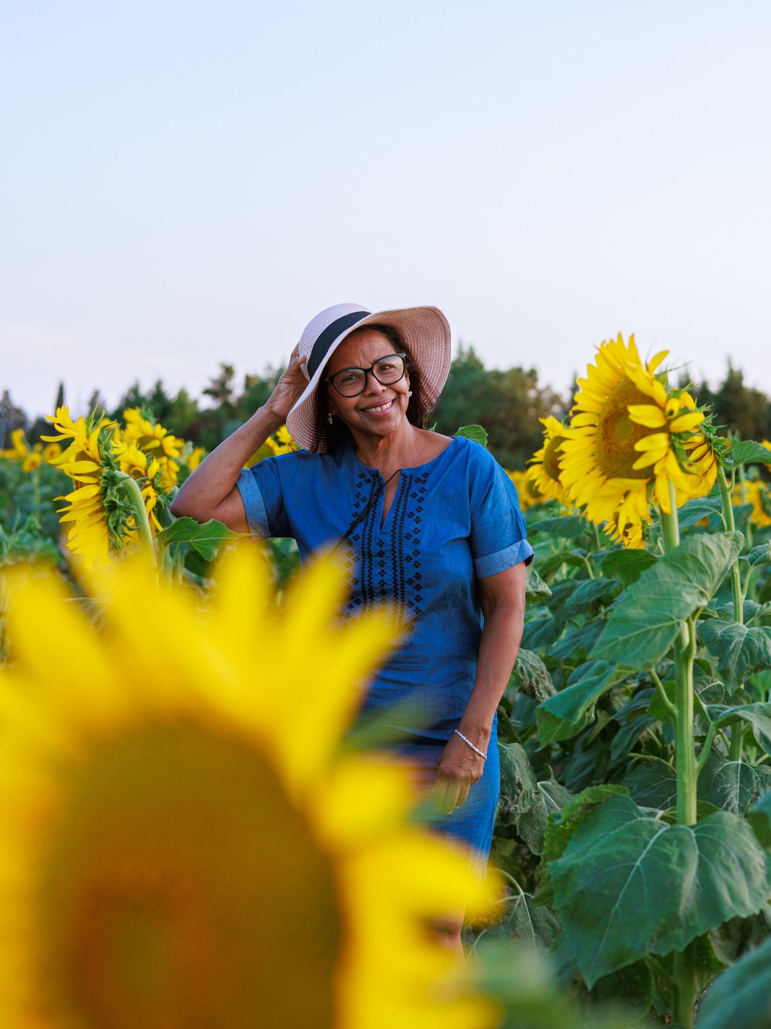 Une femme sourit au milieu d’un champ de tournesols pendant une séance photo portrait en extérieur.