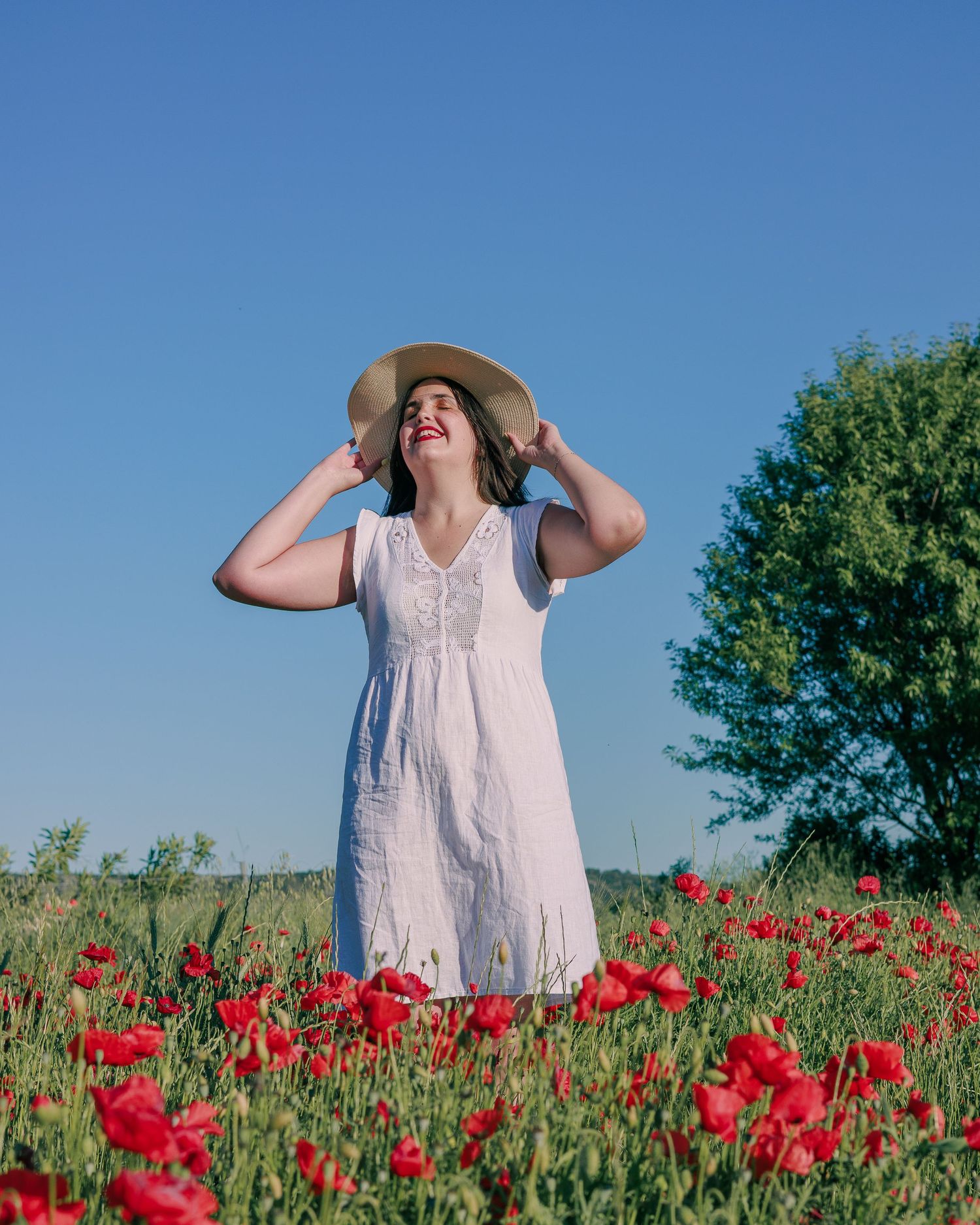 Une femme pose avec un chapeau dans un champ de coquelicots pendant une séance photo portrait a Rochefort du Gard