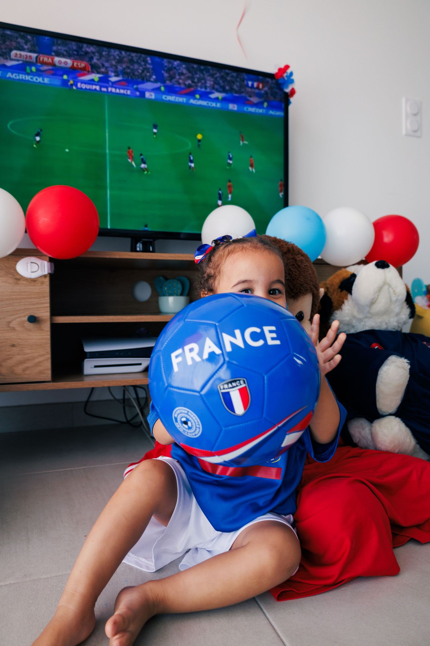 Une petite fille joue avec un ballon de football devant la télévision pendant un match de l’équipe de France.
