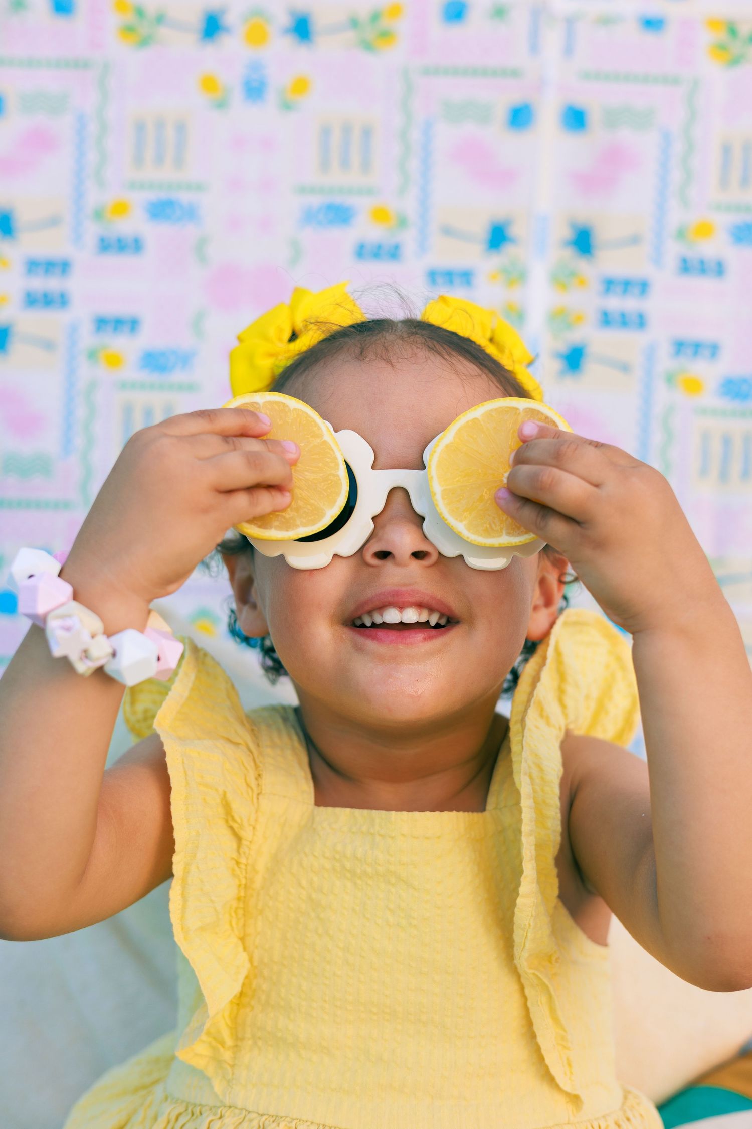 Une petite fille joue avec deux moitiés de citron devant ses yeux pendant une séance photo enfant sur le thème de l’été.