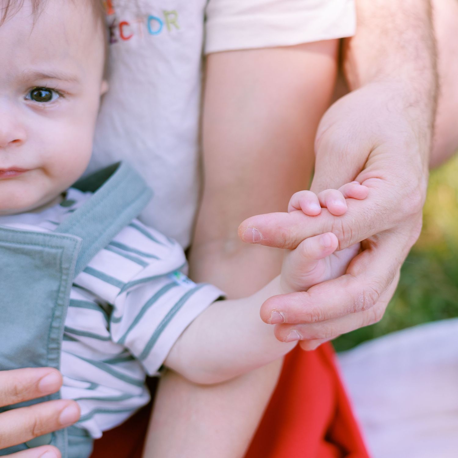 Gros plan sur la main d’un bébé tenant celle de son parent pendant une séance photo famille.