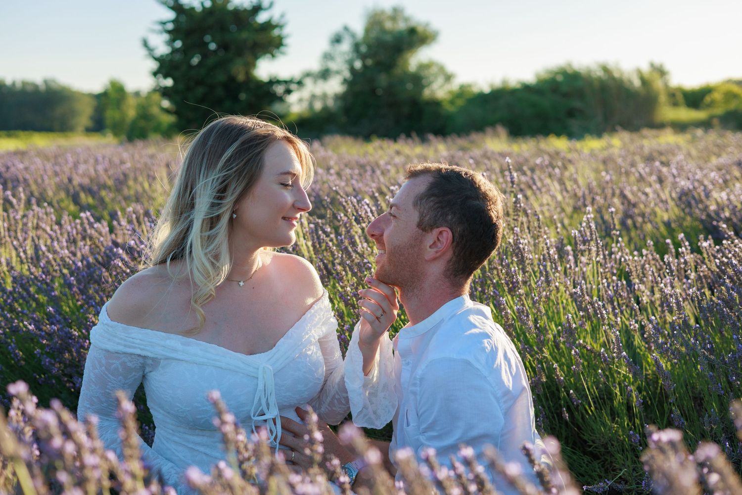 Un couple de futurs parents rit et échange un regard complice dans un champ de lavande pendant une séance photo grossesse.
