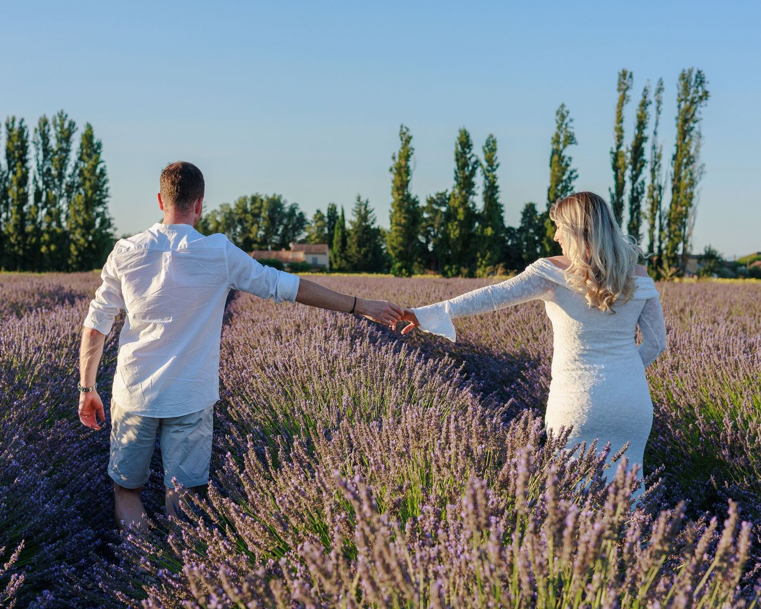 Un couple de futurs parents se tient la main en marchant dans un champ de lavande pendant une séance photo grossesse.