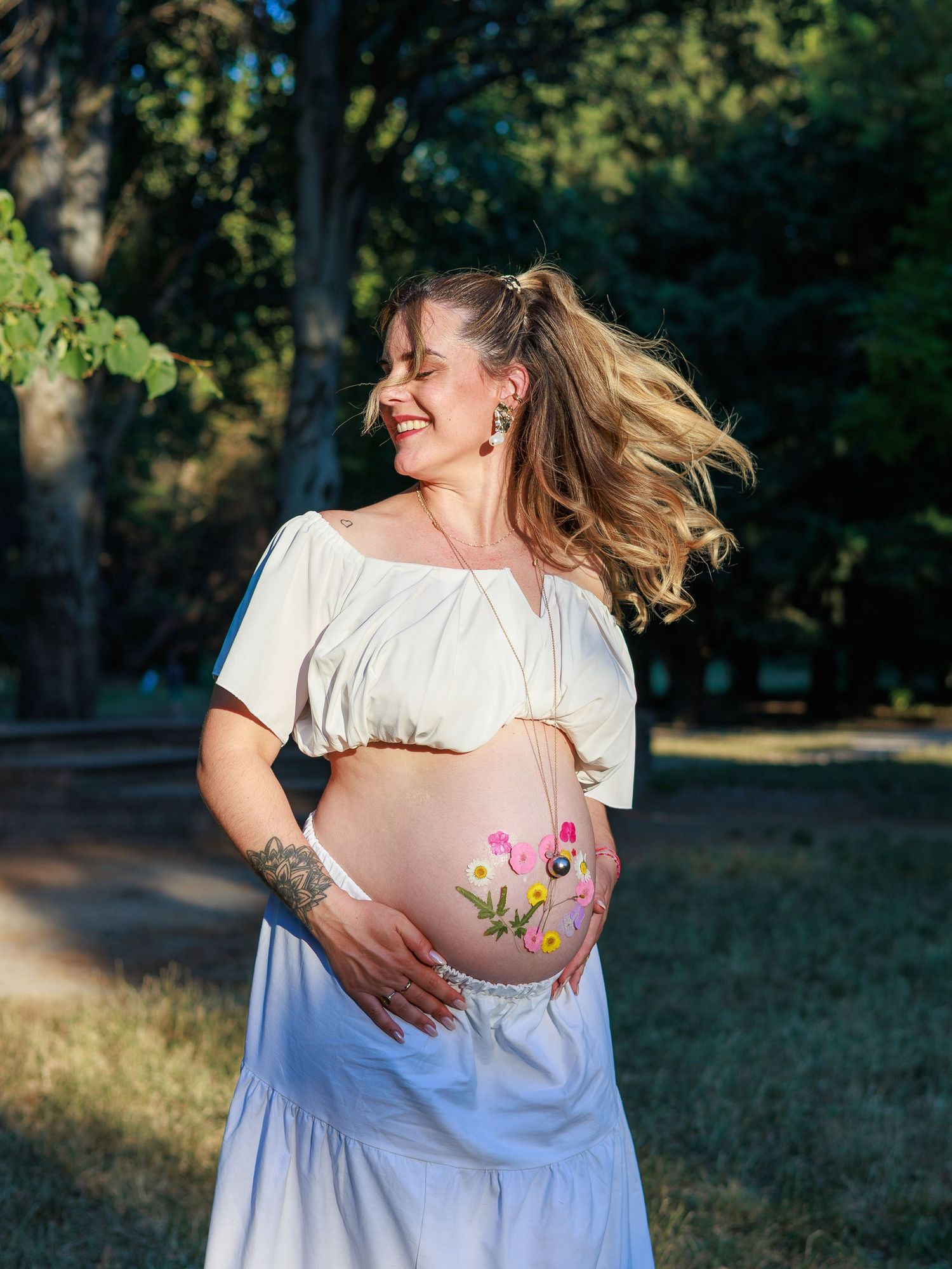 Une future maman sourit en tenant son ventre décoré de fleurs pendant une séance photo grossesse.