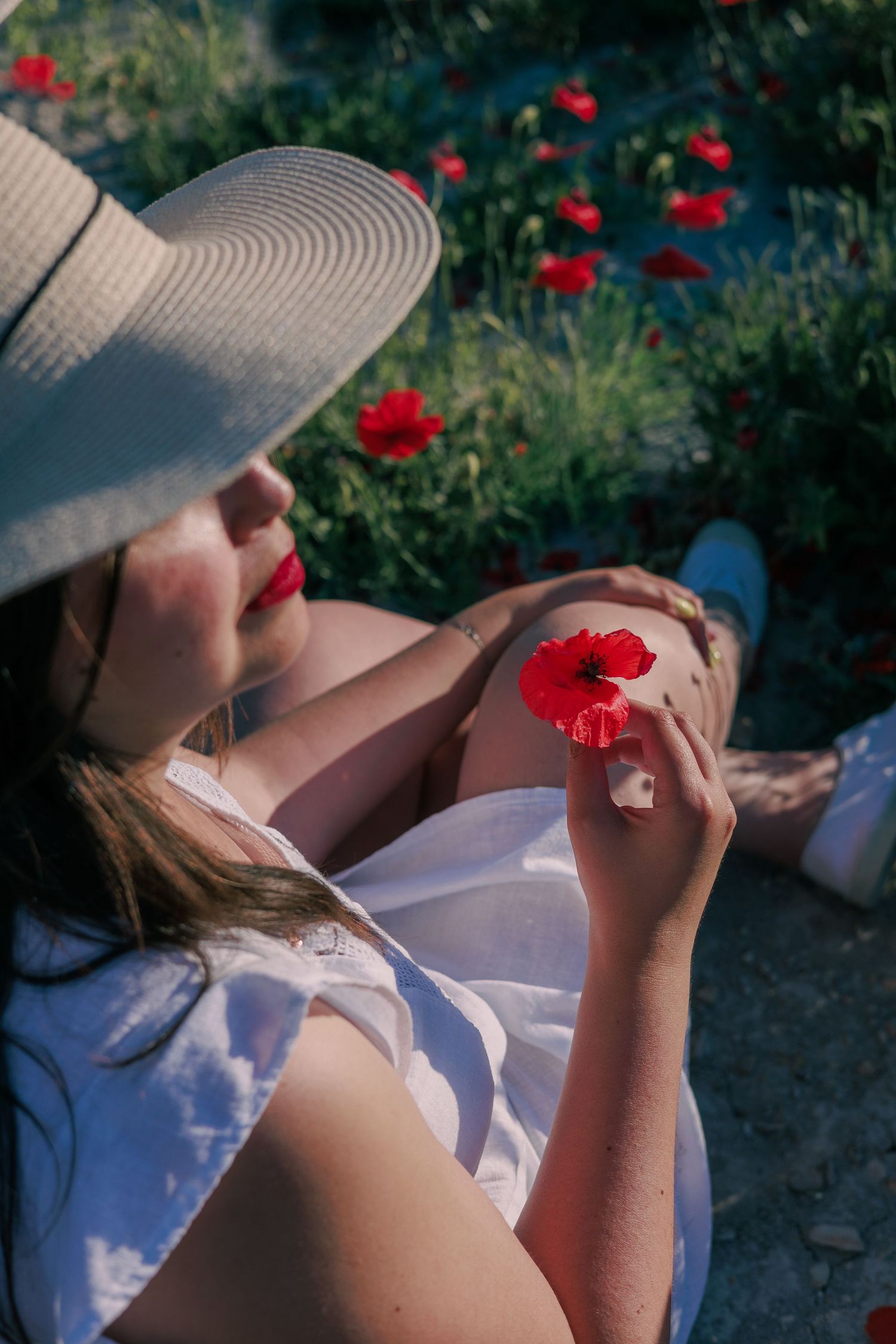 Une femme pose avec un chapeau dans un champ de coquelicots pendant une séance photo portrait en extérieur.