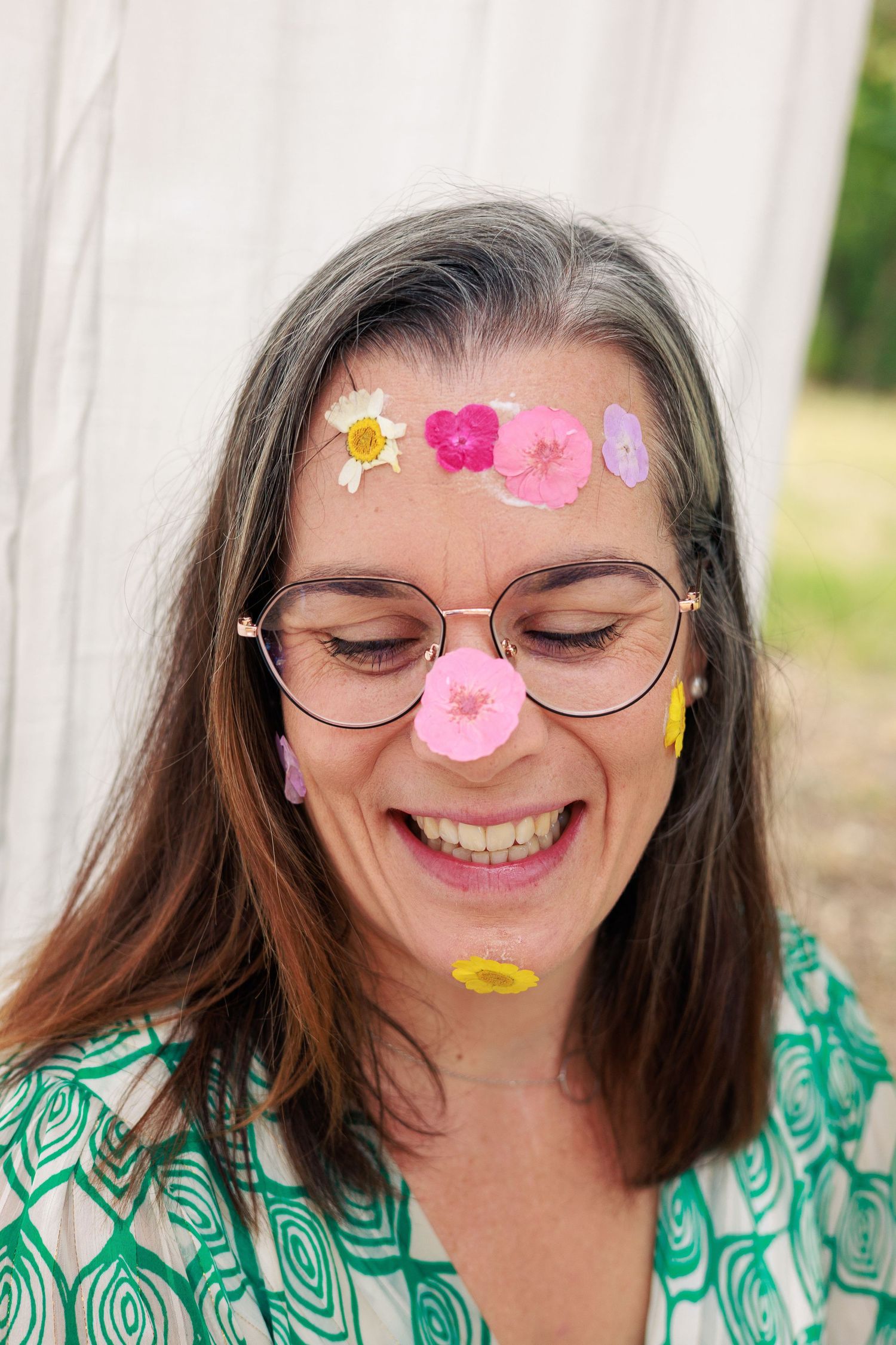 Une femme rit avec des petites fleurs posées sur le visage pendant une séance photo pleine de spontanéité.