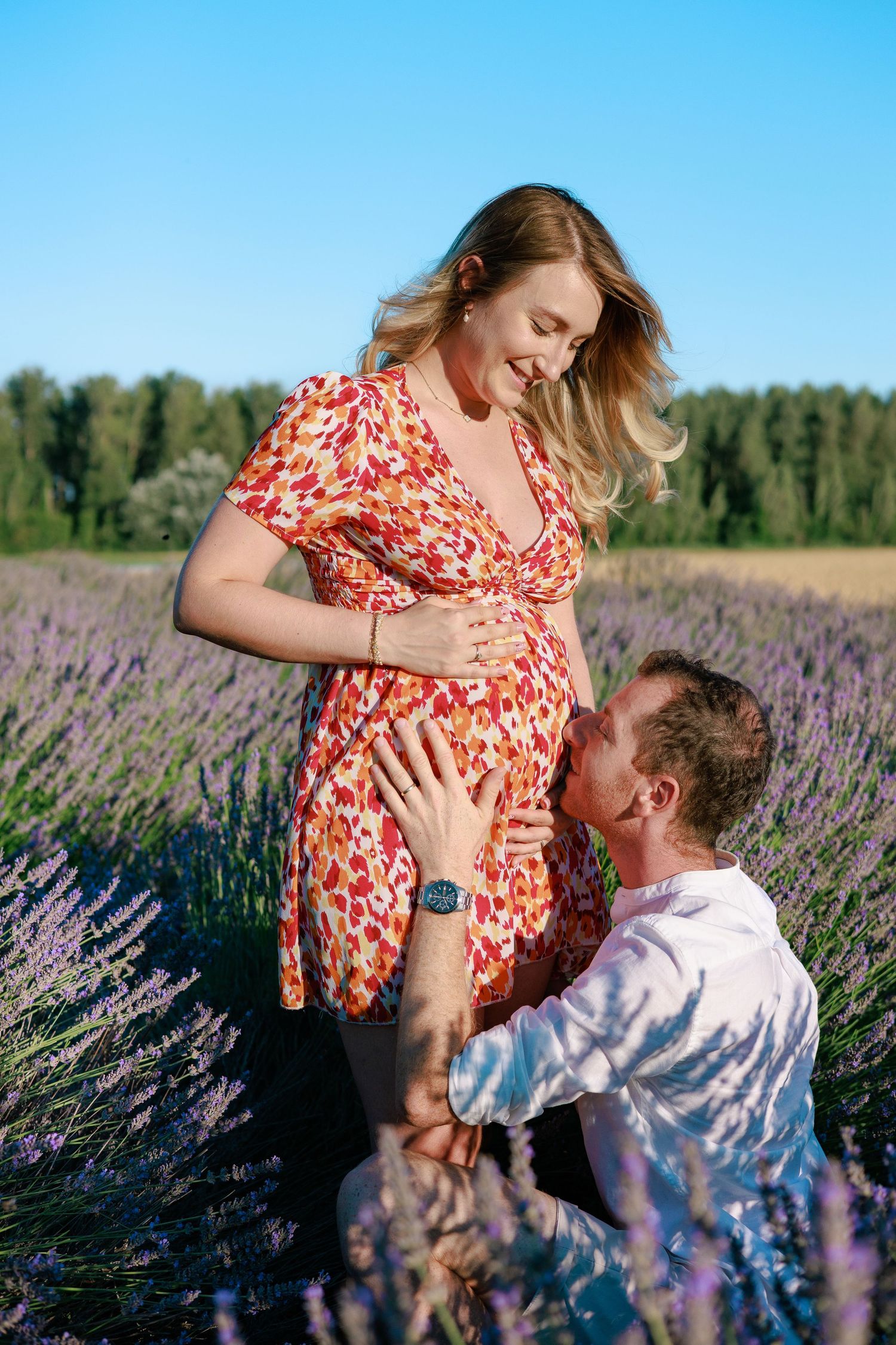 Un futur papa embrasse le ventre de sa compagne pendant une séance photo grossesse dans un champ de lavande.