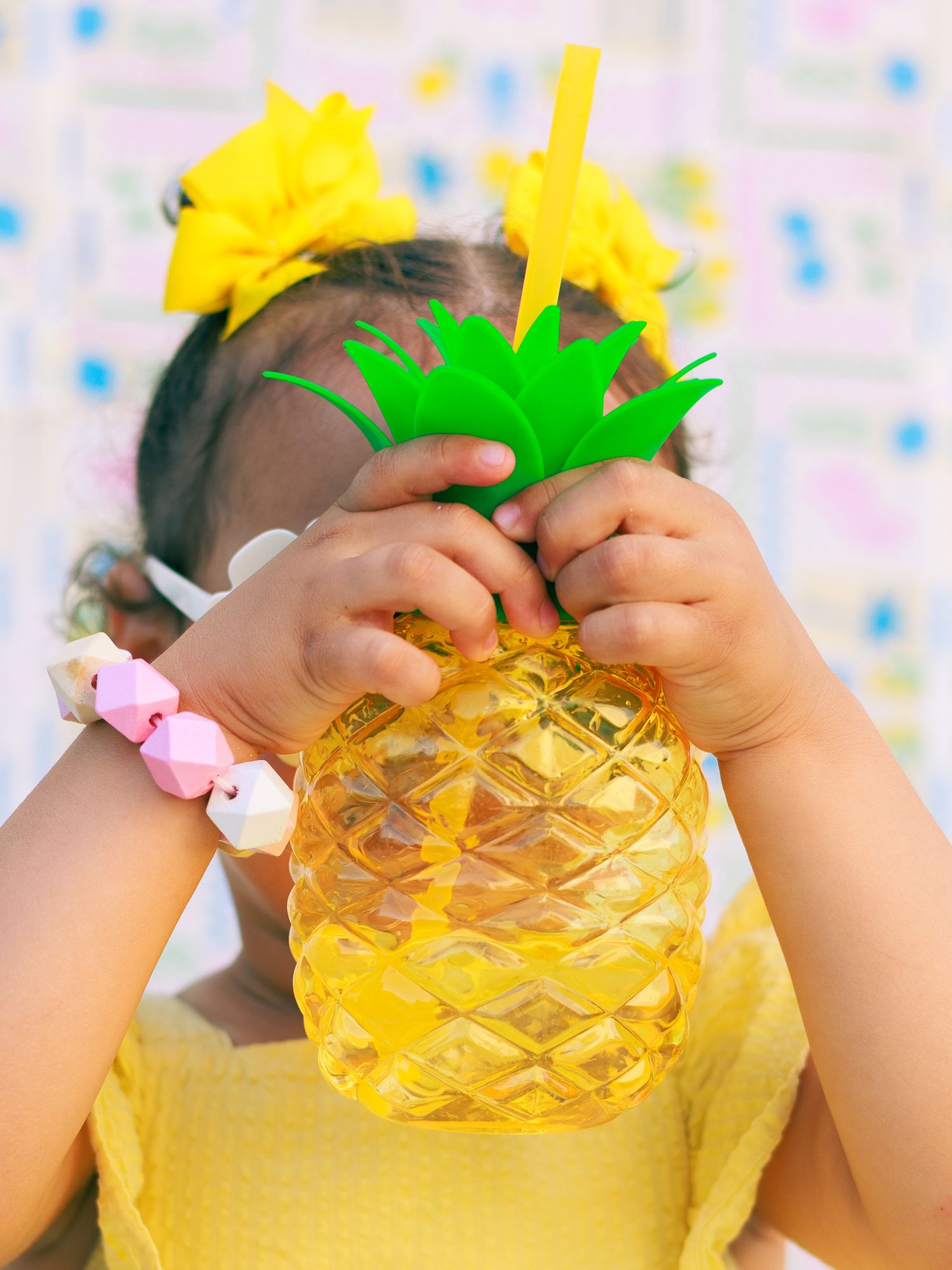 Un bébé cache son visage derrière une décoration ananas pendant une séance photo enfant.