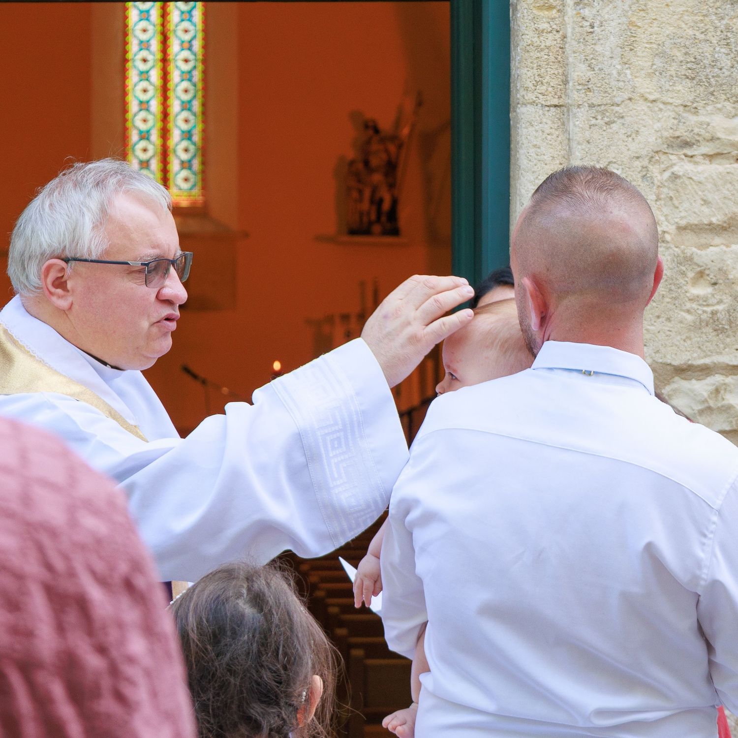 Un prêtre bénit un participant devant l’église pendant une cérémonie de baptême.