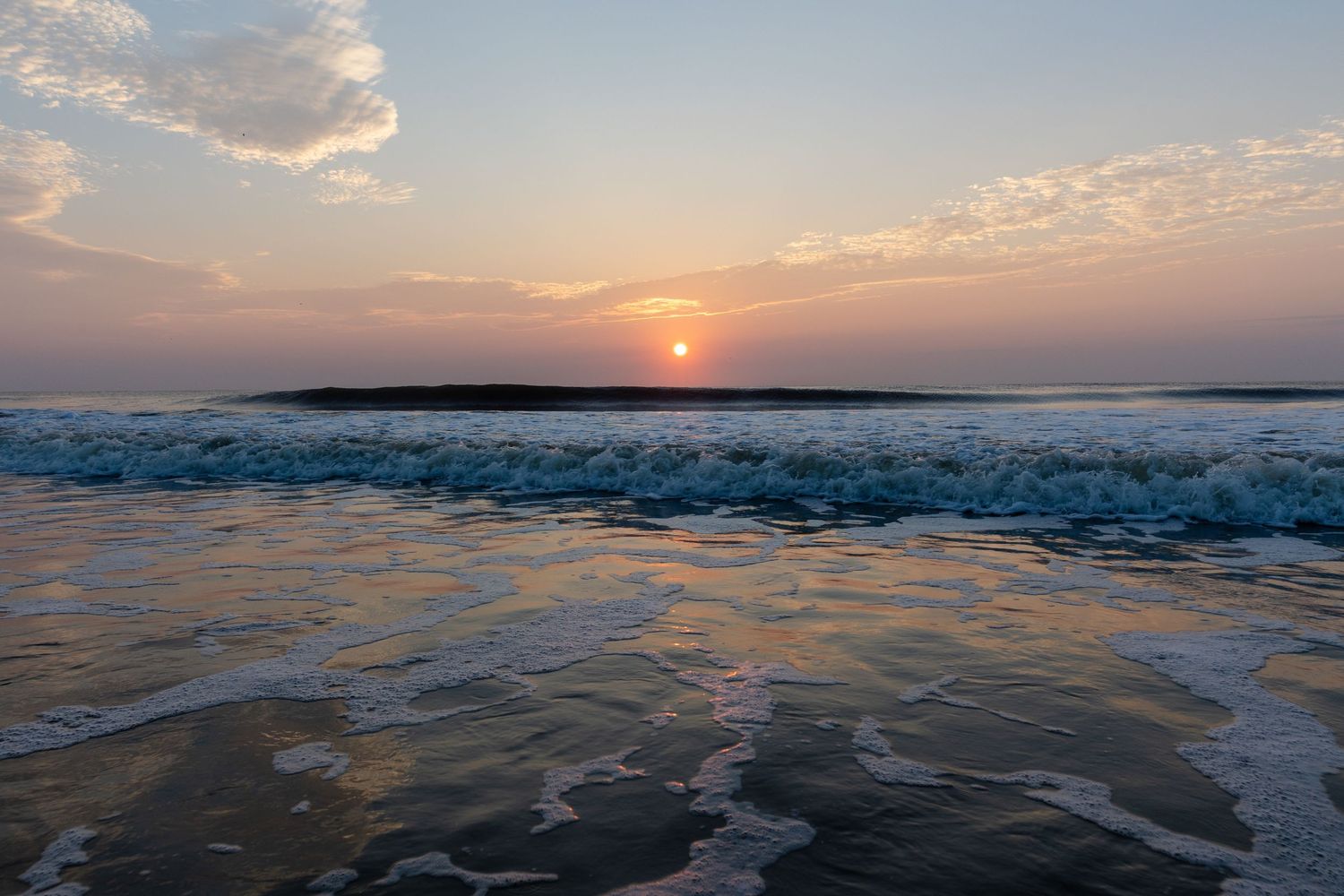 Dramatic ocean sunset with rolling waves crashing on beach as golden sun dips below horizon over sea.