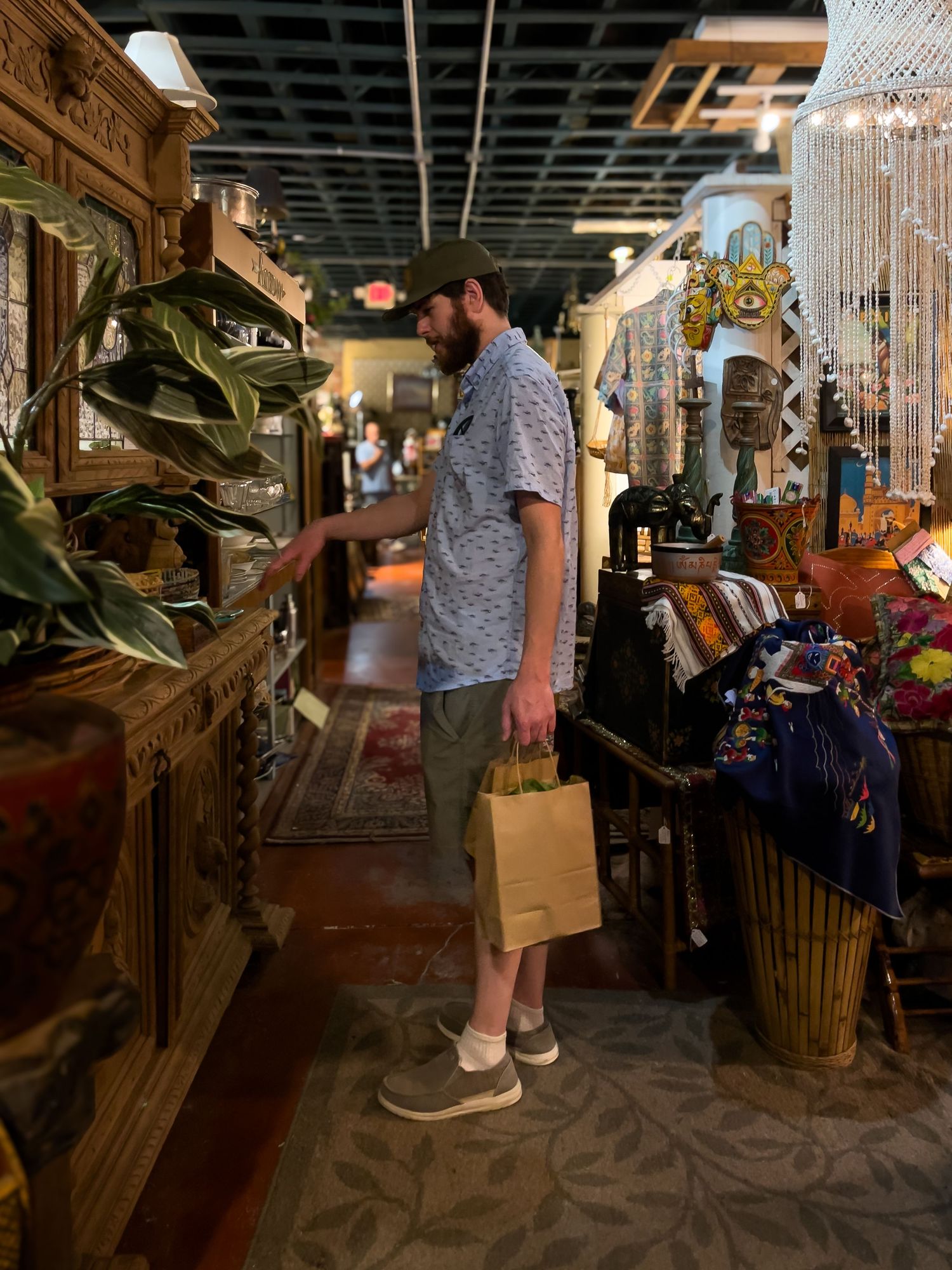 Customer browsing in an eclectic shop filled with plants, decor, and vintage furnishings in a dimly lit space.