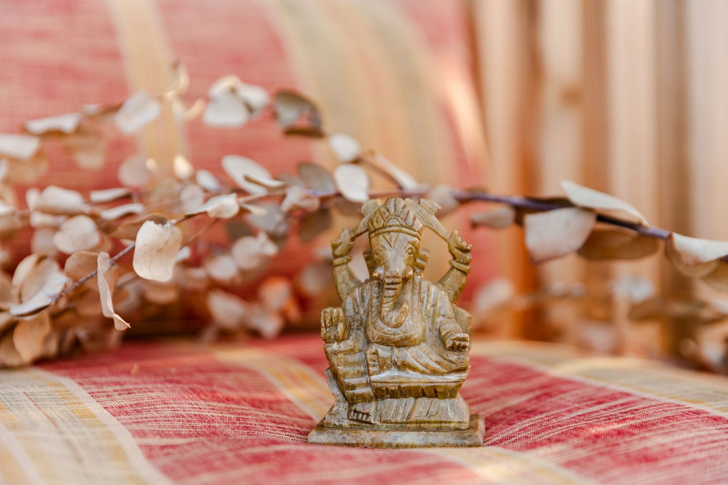 Small decorative Ganesha statue displayed on red textured fabric with dried floral accents.