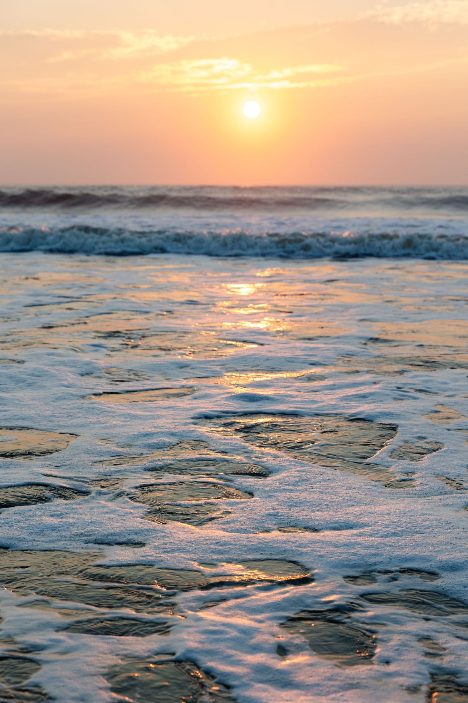 Golden sunset over the ocean with waves crashing and water reflecting warm light on textured wet sand.