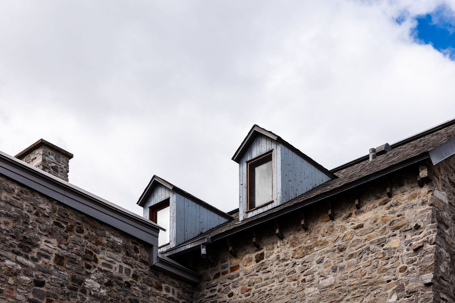 Stone building with three dormer windows on a traditional pitched roof against cloudy sky.