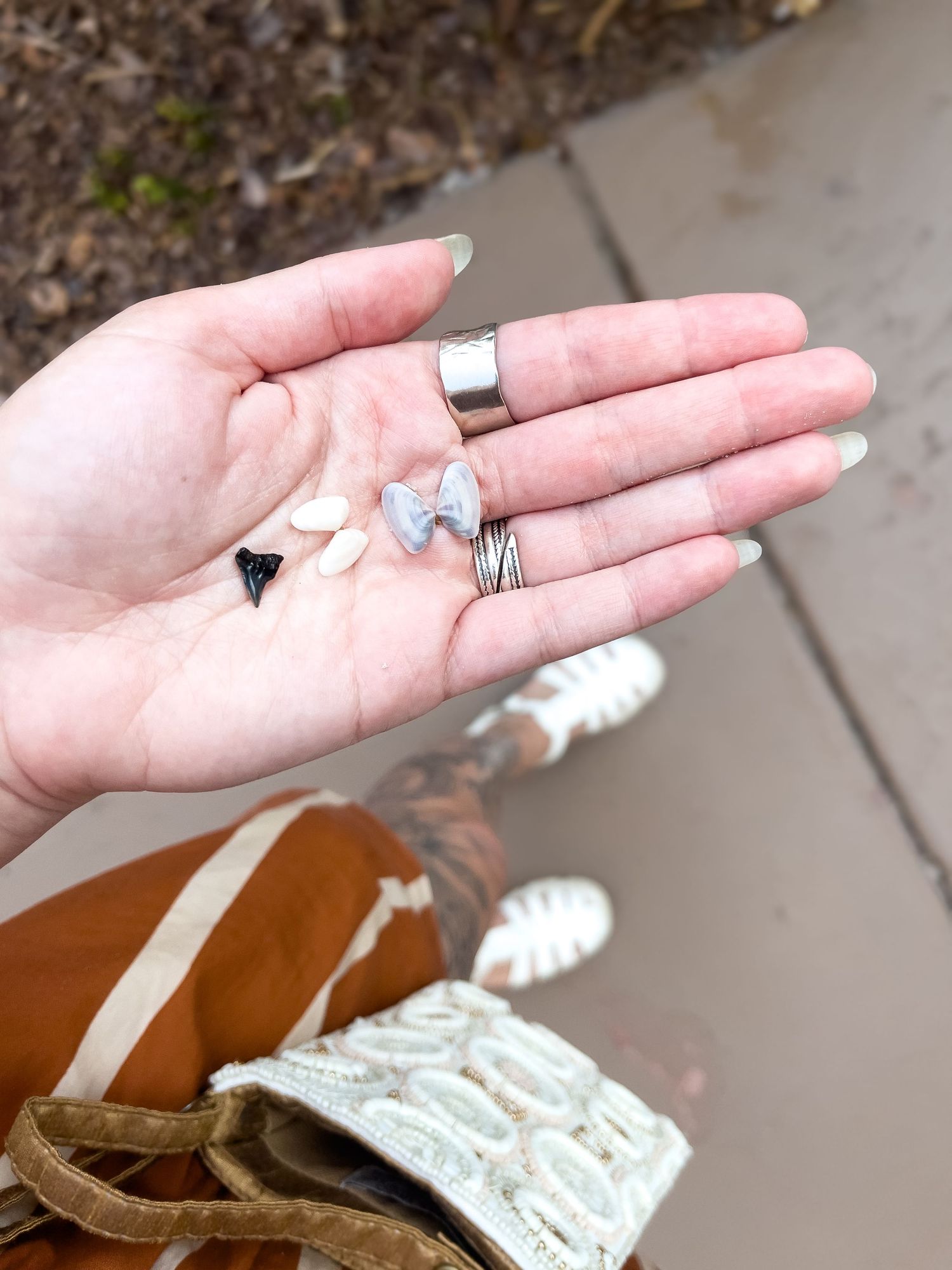 A palm holds several small silver rings and crystals while wearing denim and brown leather accessories.