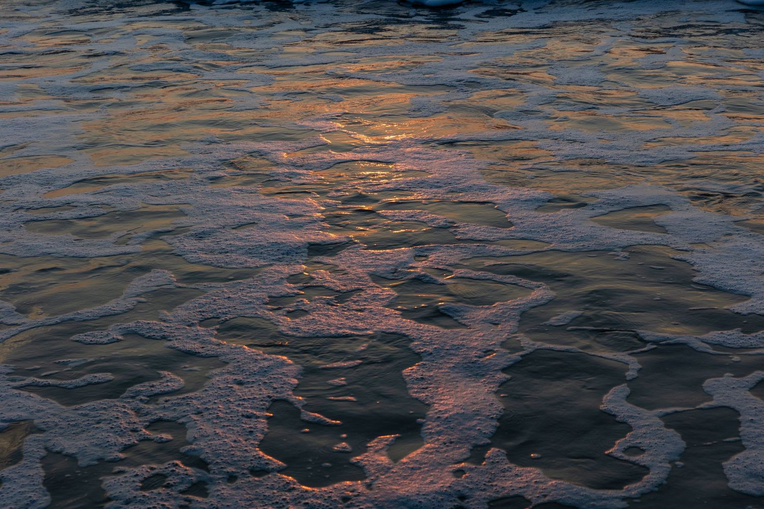 Sunset reflects orange and pink hues on dark rippling water surface creating a mesmerizing pattern.