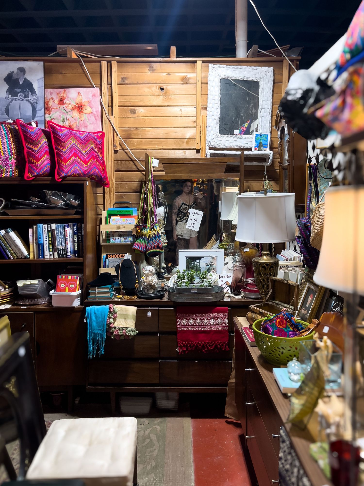 Cozy vintage shop interior with wooden shelves displaying colorful pillows, lamps, books and various home decor items.