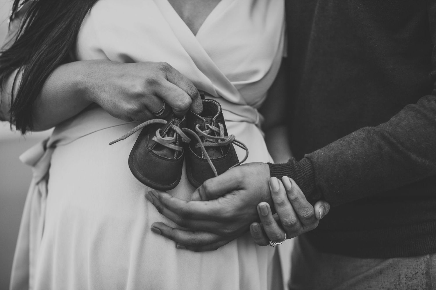 Black and white photo of couple holding tiny baby shoes over pregnant belly.
