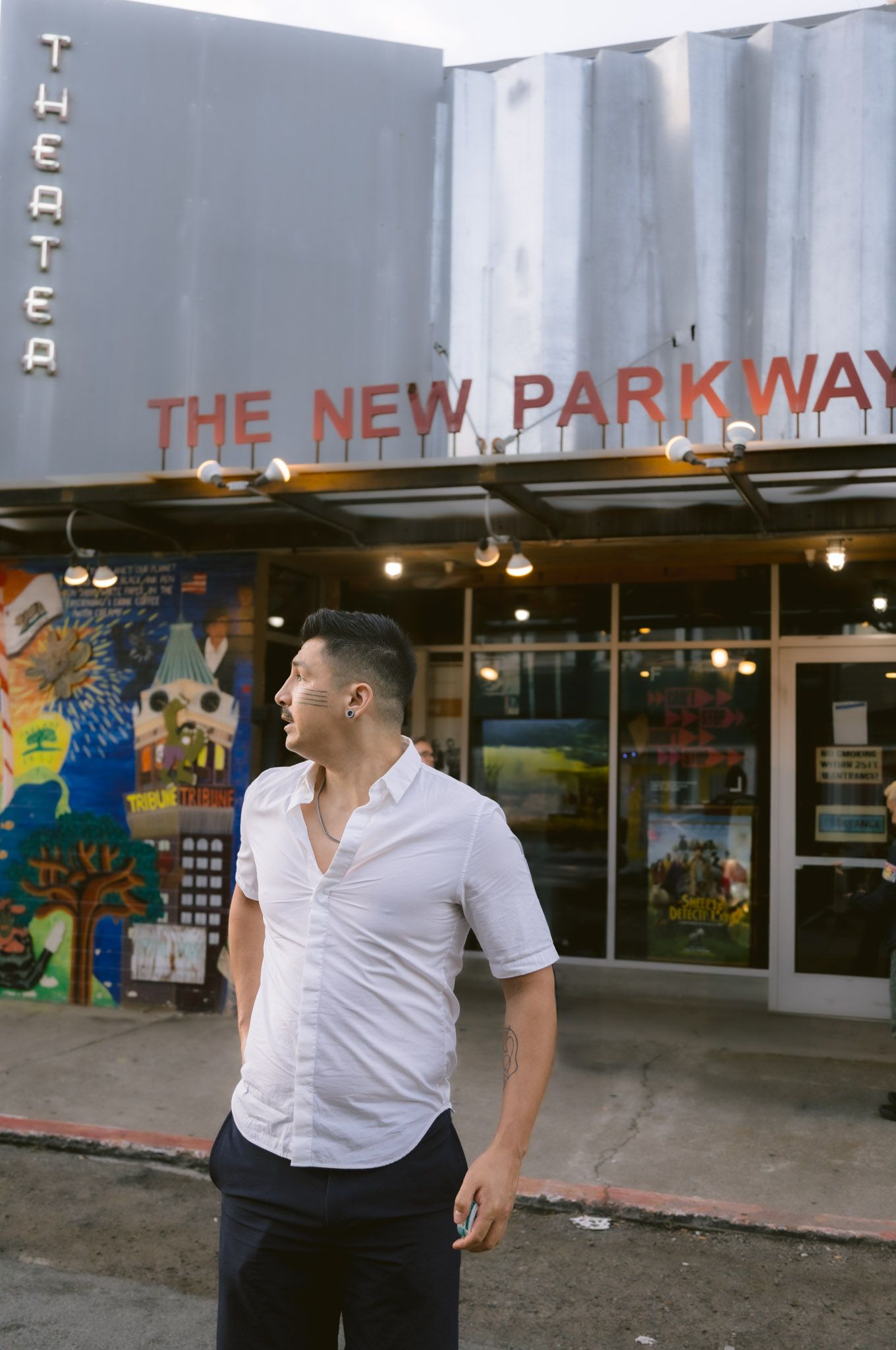 Man in white shirt standing outside The New Parkway Theater with colorful murals in Oakland, CA.