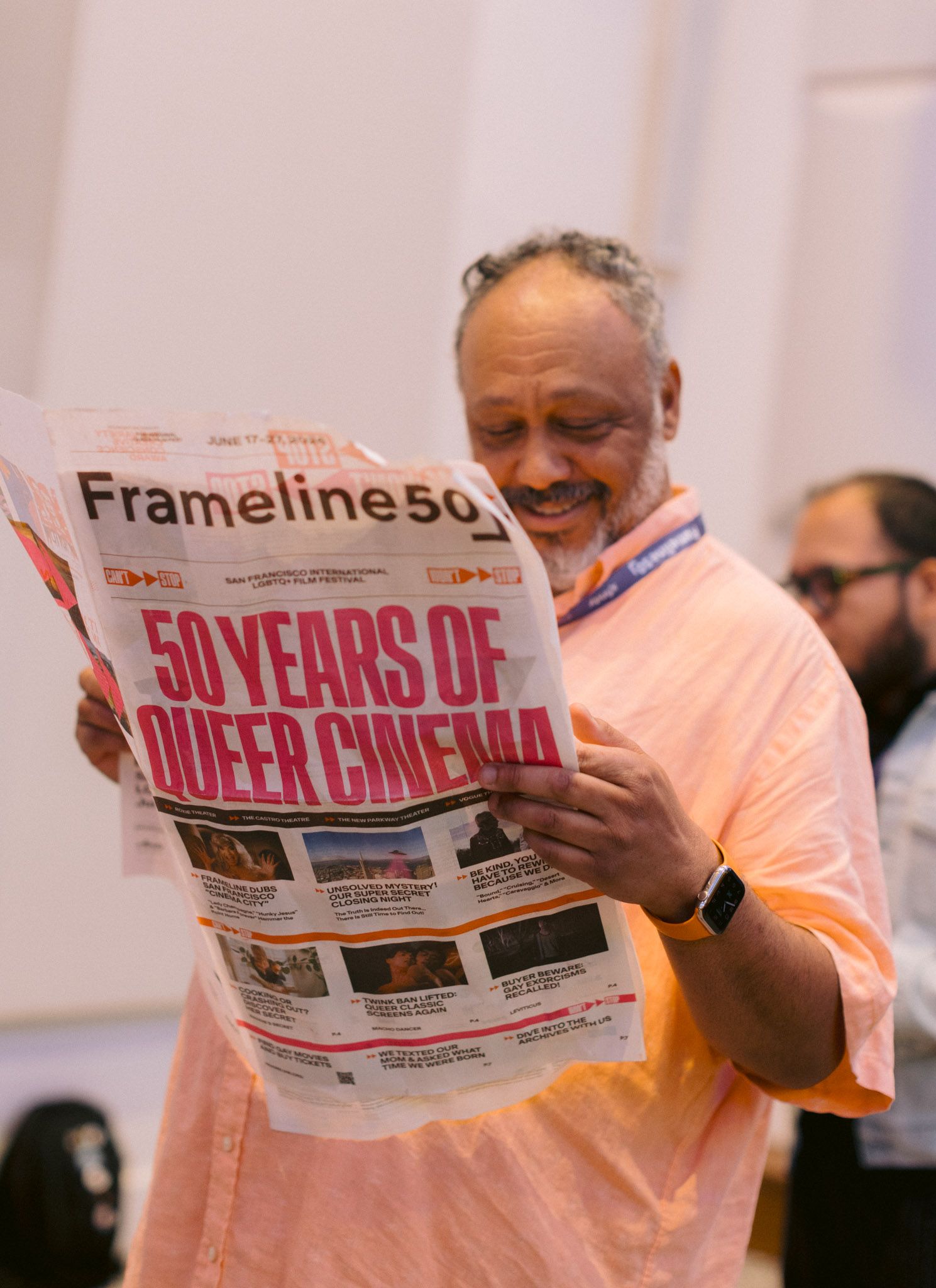 Man smiling while reading Frameline50 newspaper headline 50 Years of Queer Cinema at LGBTQ film festival.