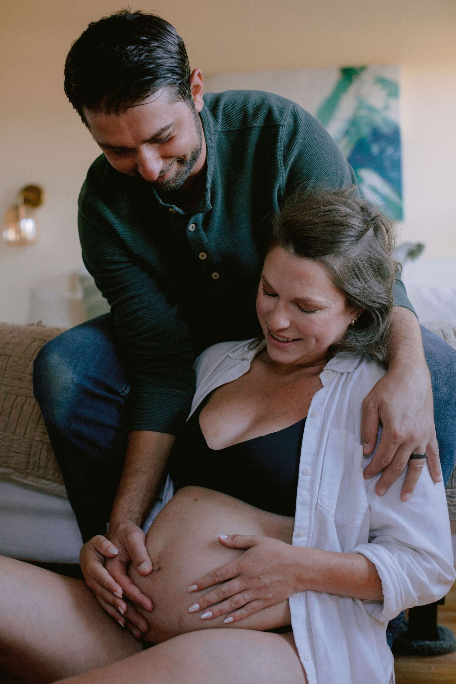 Smiling couple bonding over pregnant belly in cozy warmly lit living room.