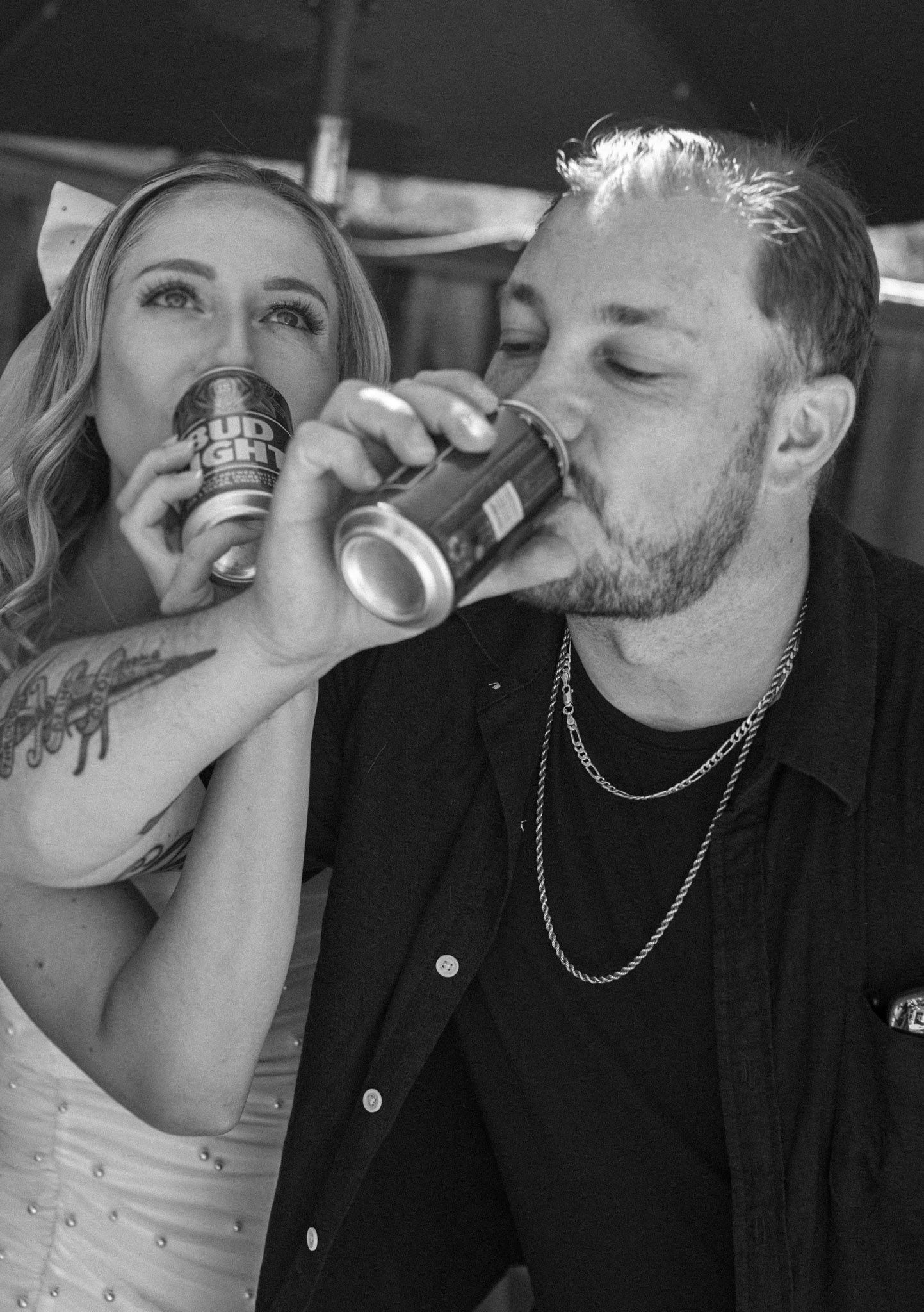 Black and white photo of a couple drinking canned beer together, woman with tattoos in white dress, man in black shirt.