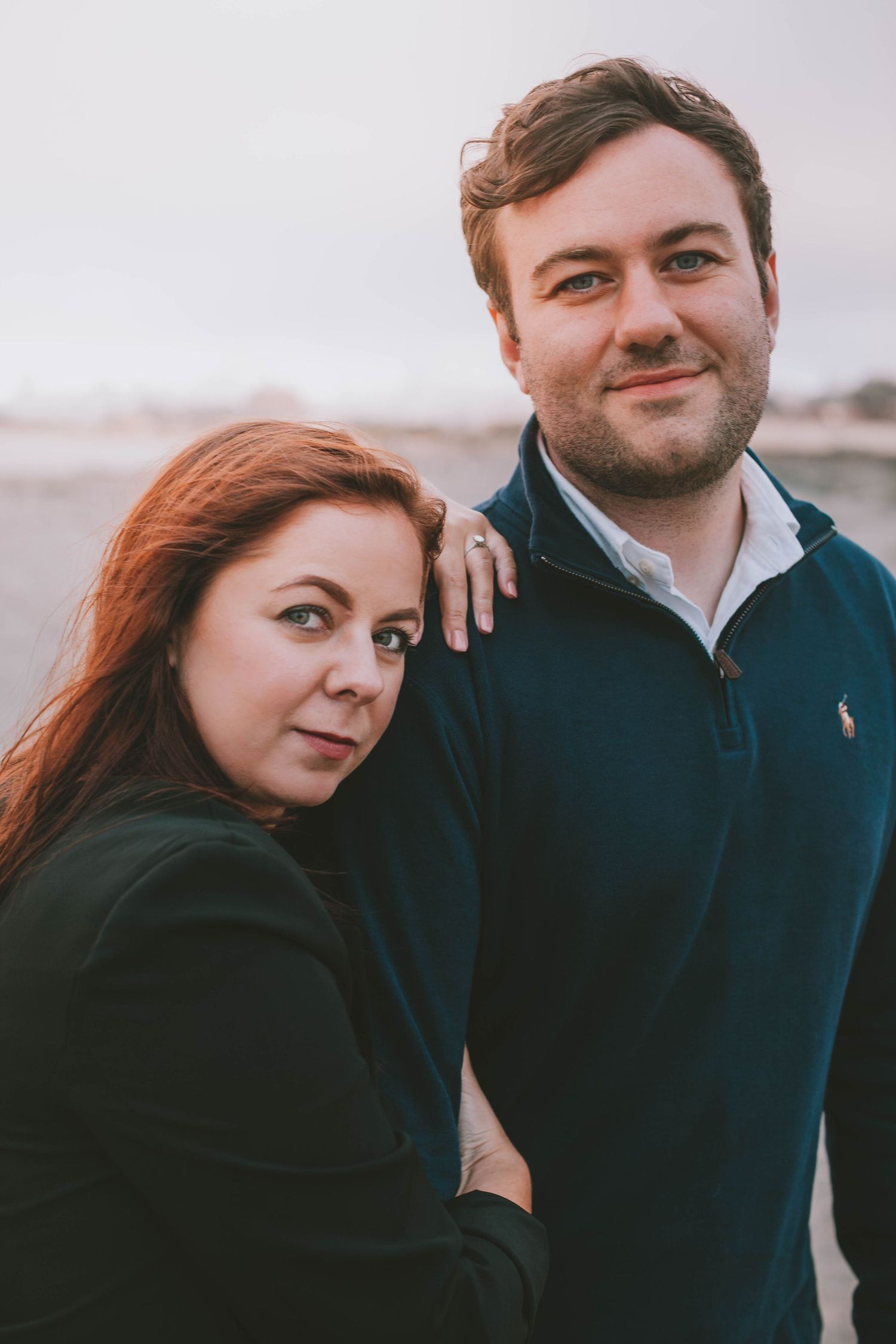 Red-haired woman and man in blue pullover posing together on beach.