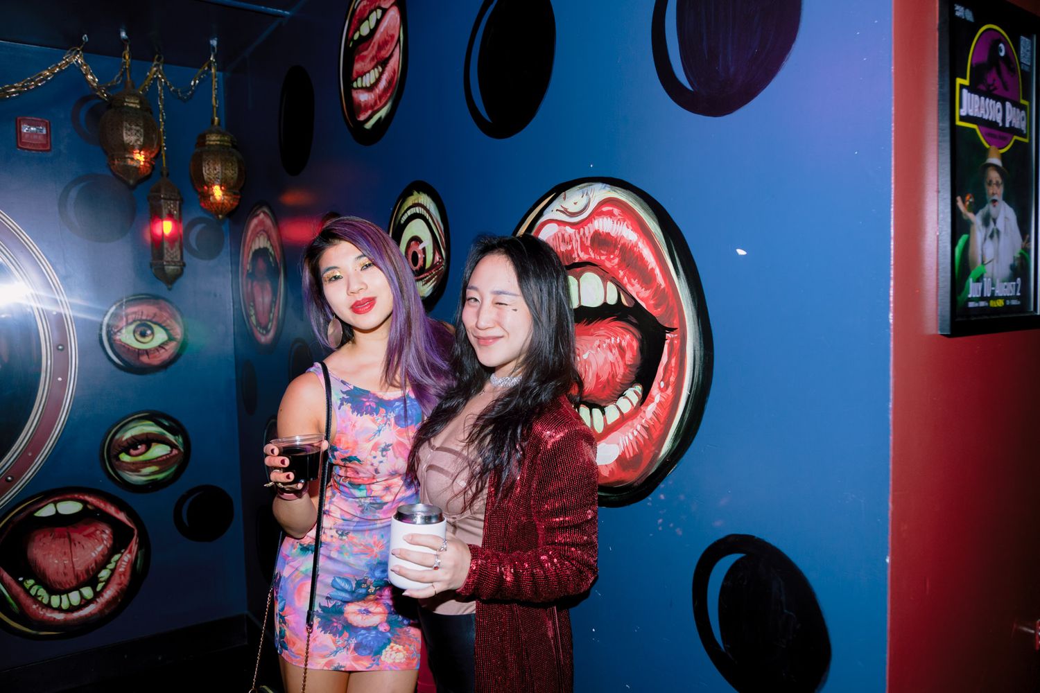 Two women smiling together in colorful pop art themed nightclub interior.