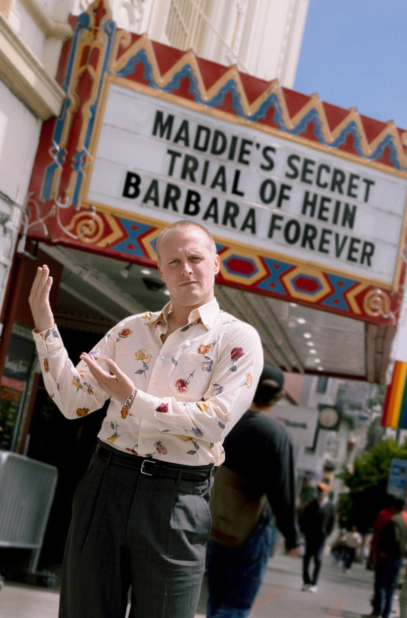 Man posing in front of theater marquee displaying Maddie's Secret Trial of Hein Barbara Forever.
