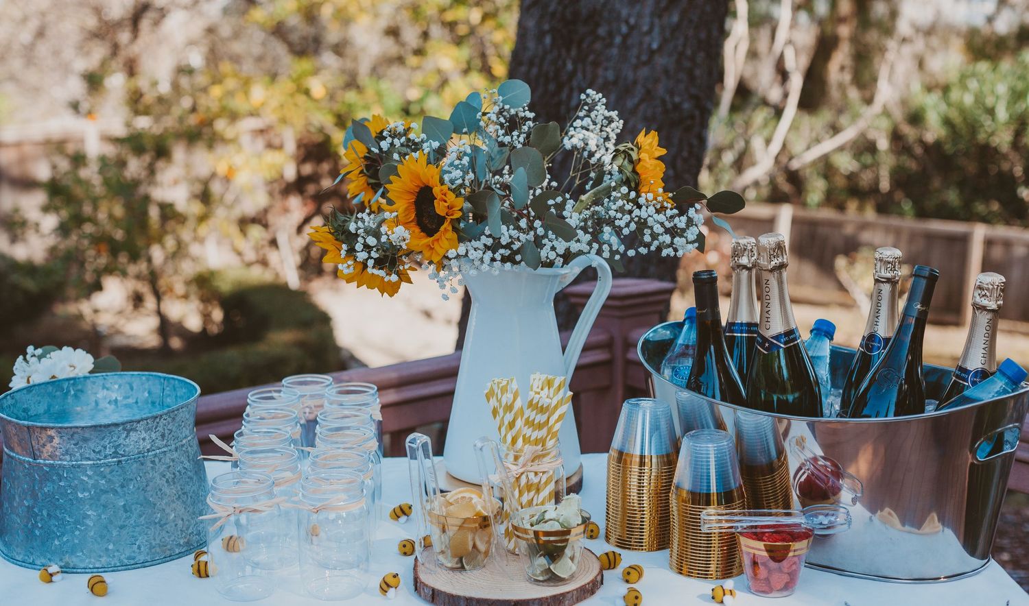 Outdoor party table with sunflower centerpiece, champagne bucket, and glassware display.