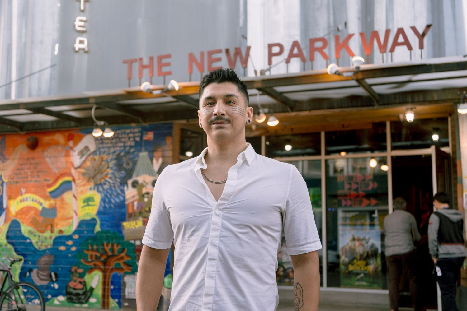 Man in white shirt standing outside The New Parkway theater with colorful mural in Oakland, CA.