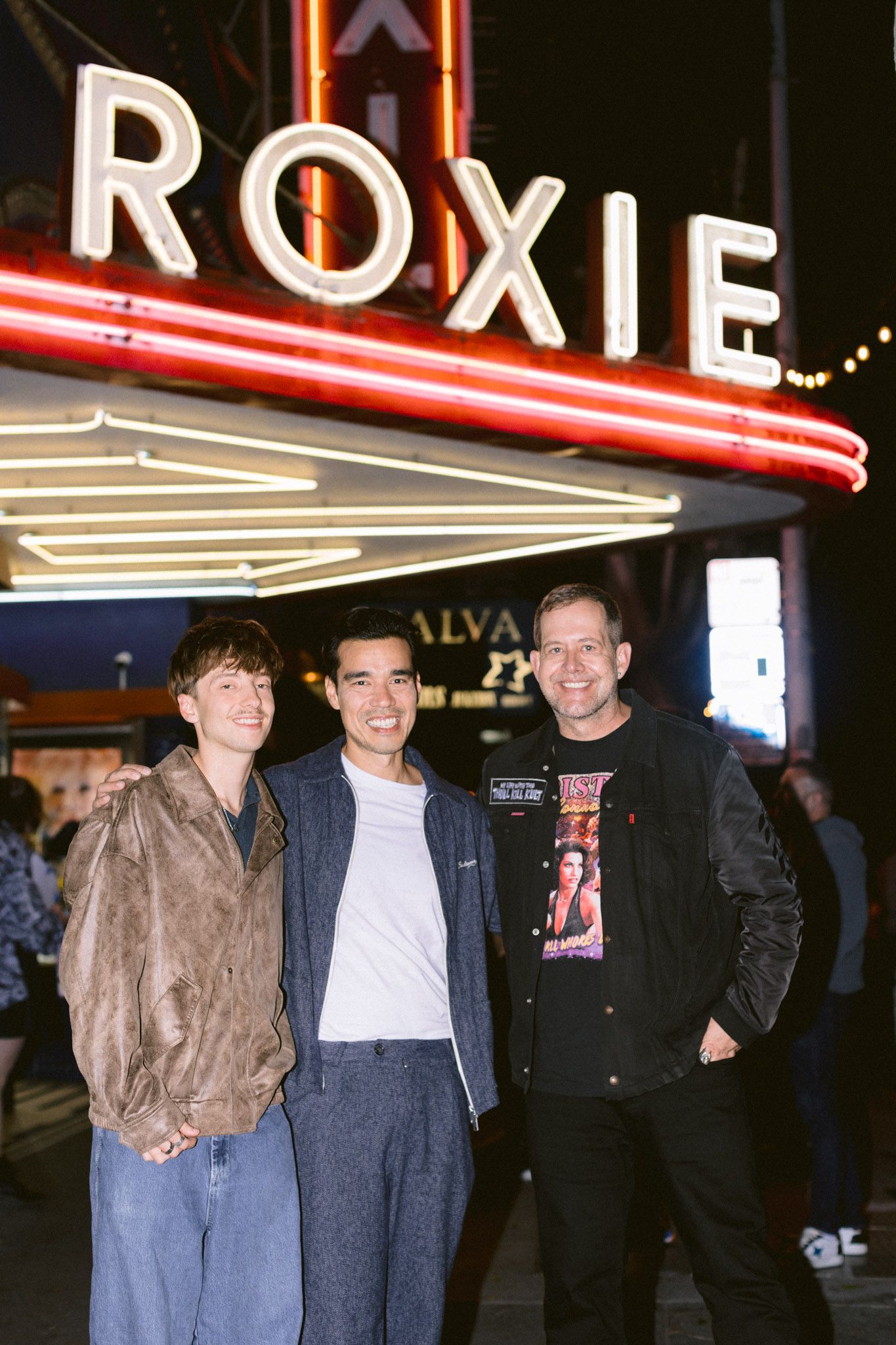 Three men posing together under the illuminated Roxie Theater marquee at night in San Francisco for the film Leviticus.