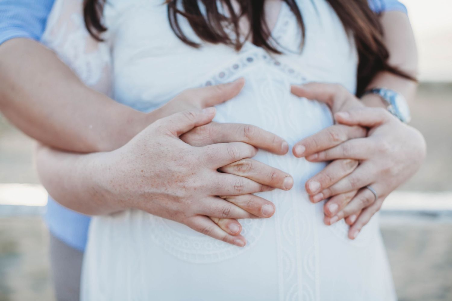 Couple forming heart shape with hands on pregnant woman's belly outdoors.
