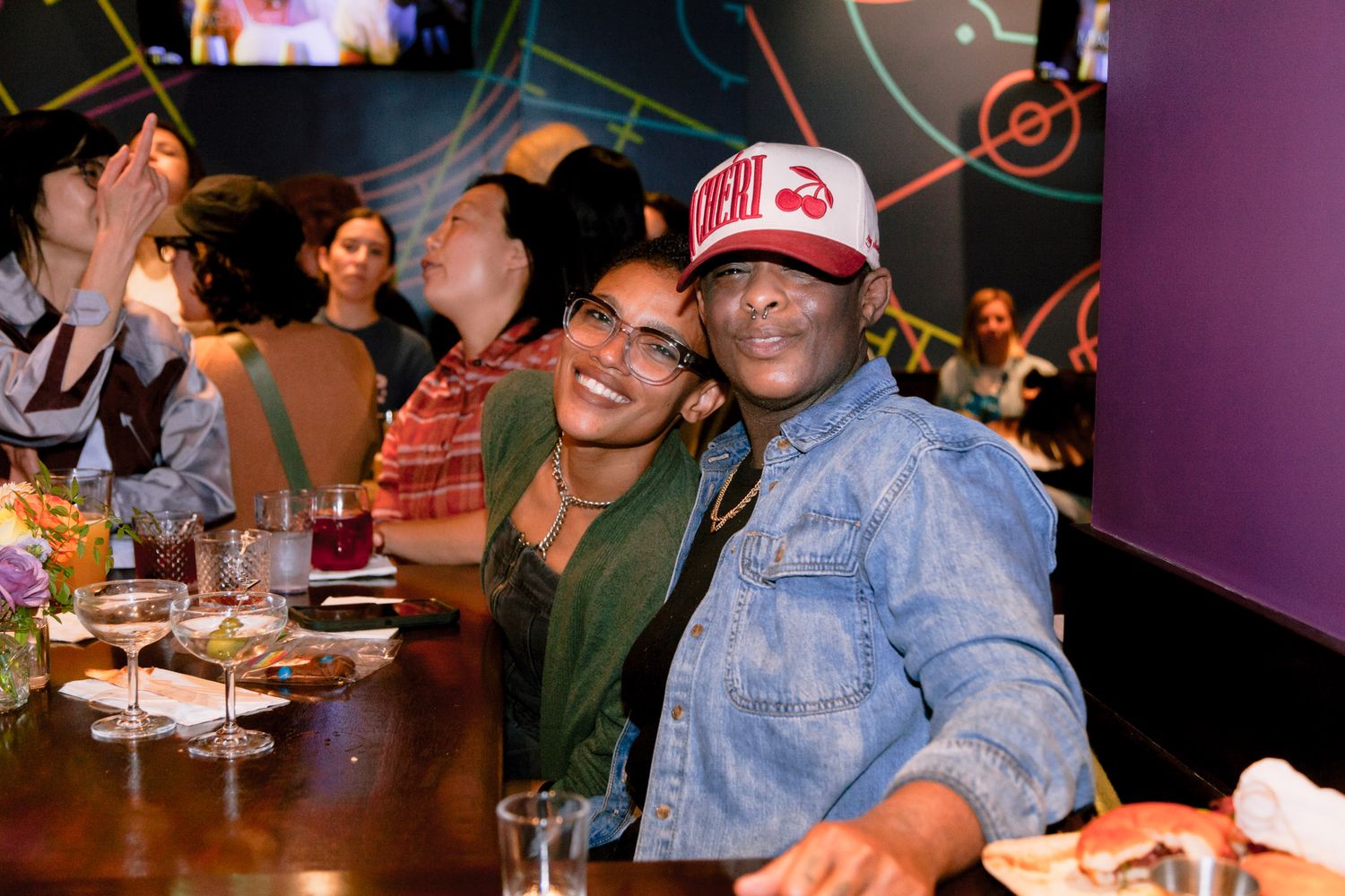 A smiling couple poses together at a bar during a lively indoor social event.