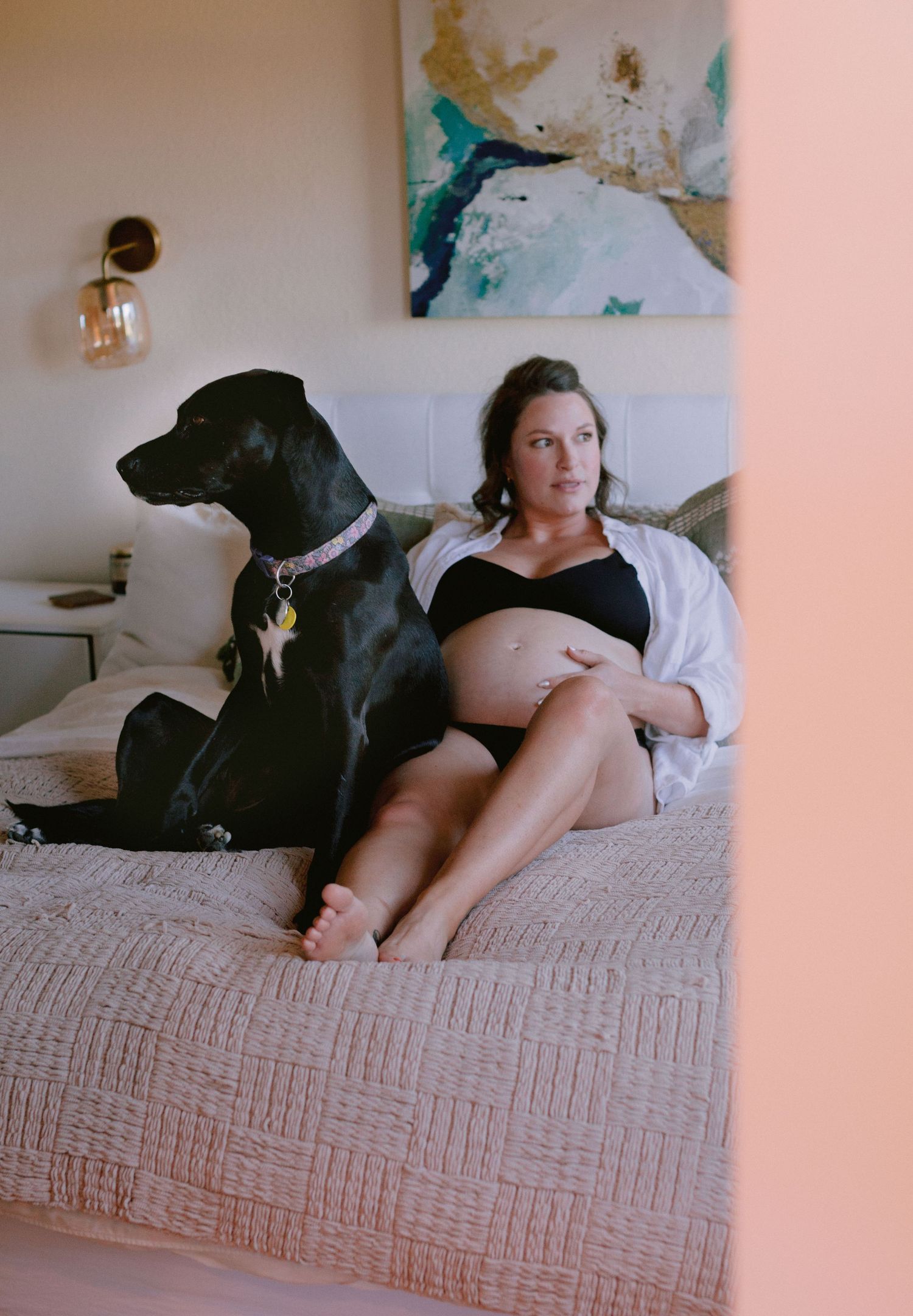 Pregnant woman relaxing on bed with large black Great Dane dog beside her.