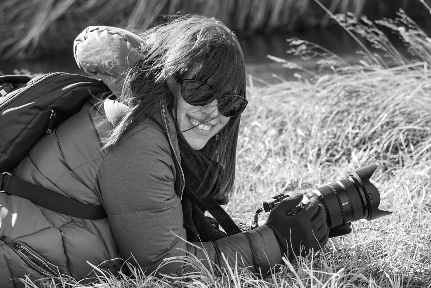 Photographer lying in a grassy field with a camera during an outdoor pet photography session.