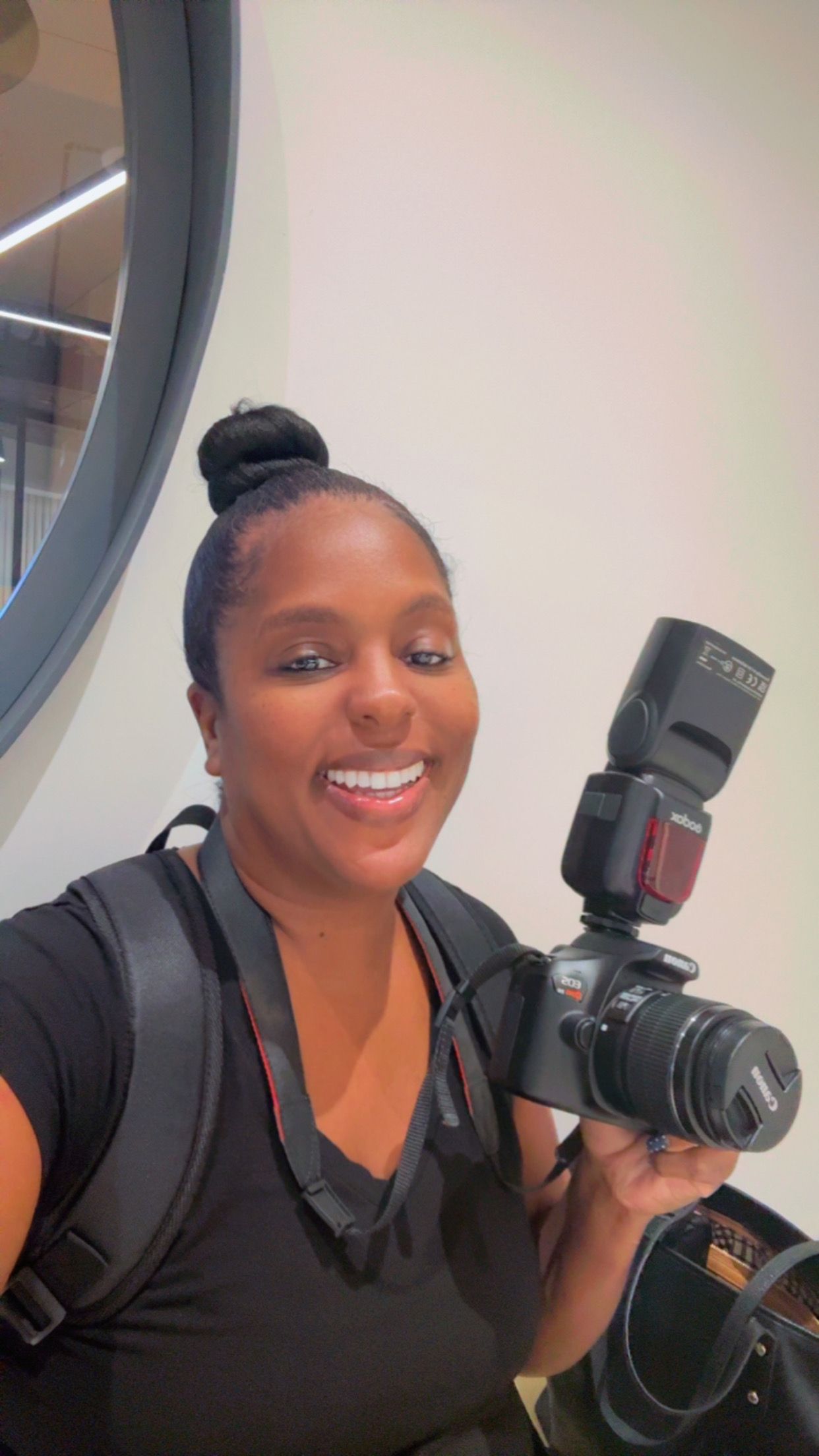 Smiling woman photographer holding a Canon DSLR camera with flash attachment.