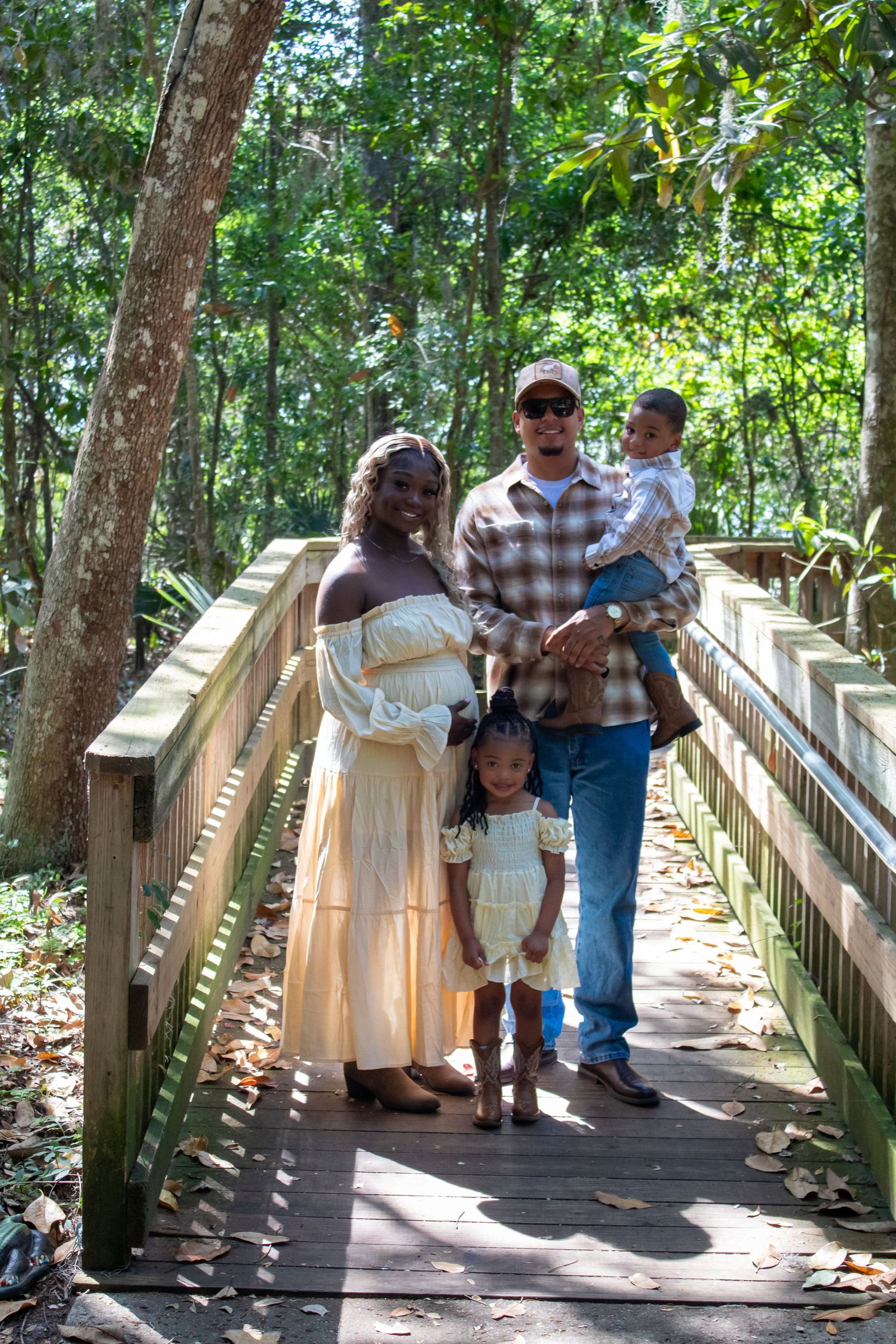 Happy interracial family of four poses on wooden bridge surrounded by green forest.