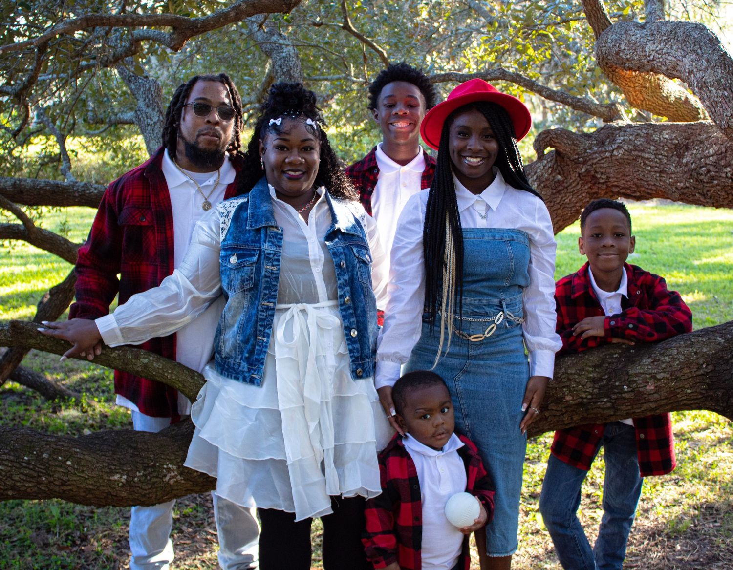 Black family of six posing together on a tree branch in coordinating outfits outdoors.