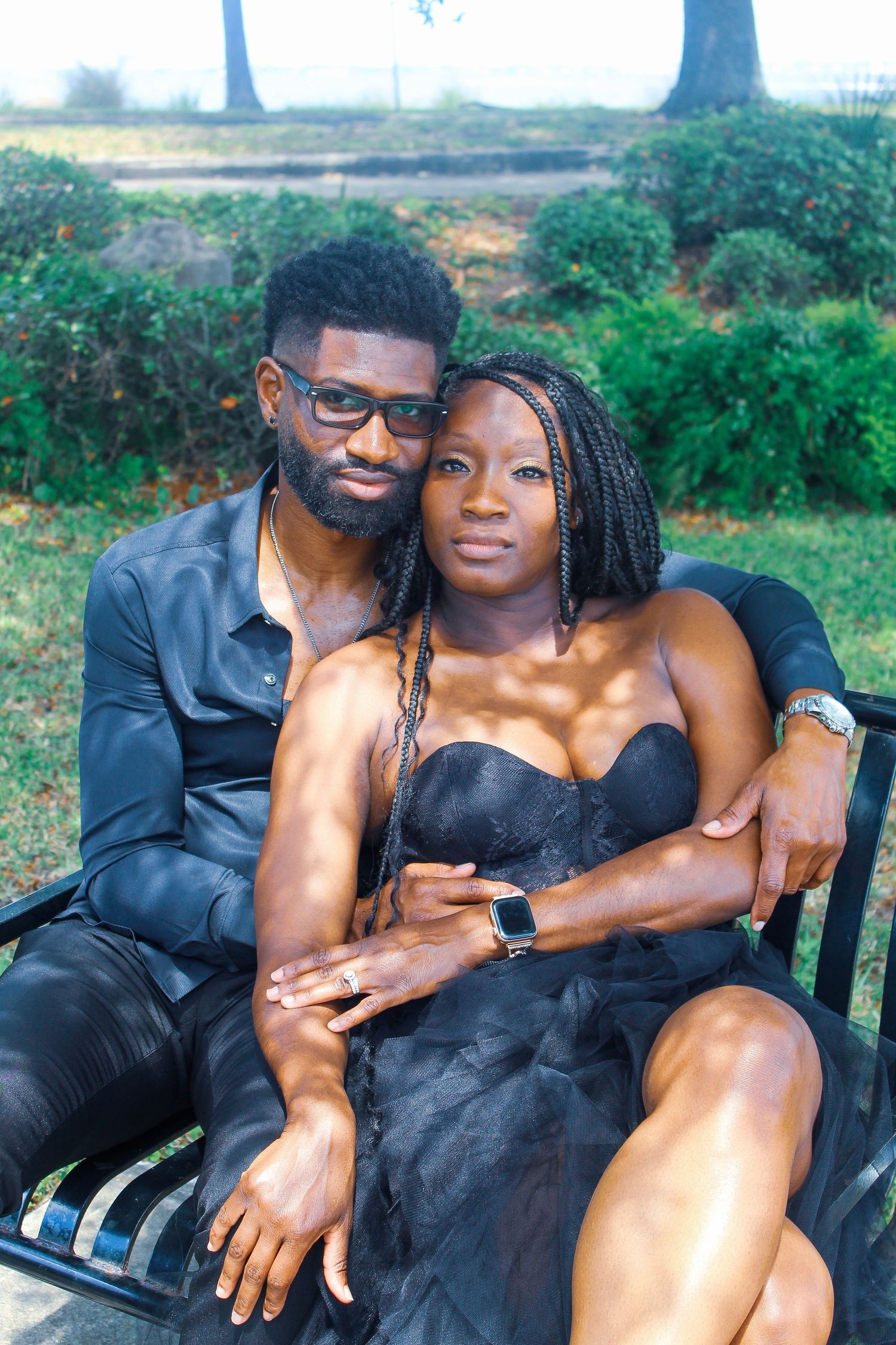 Couple dressed in black sitting closely together on a bench in a park.