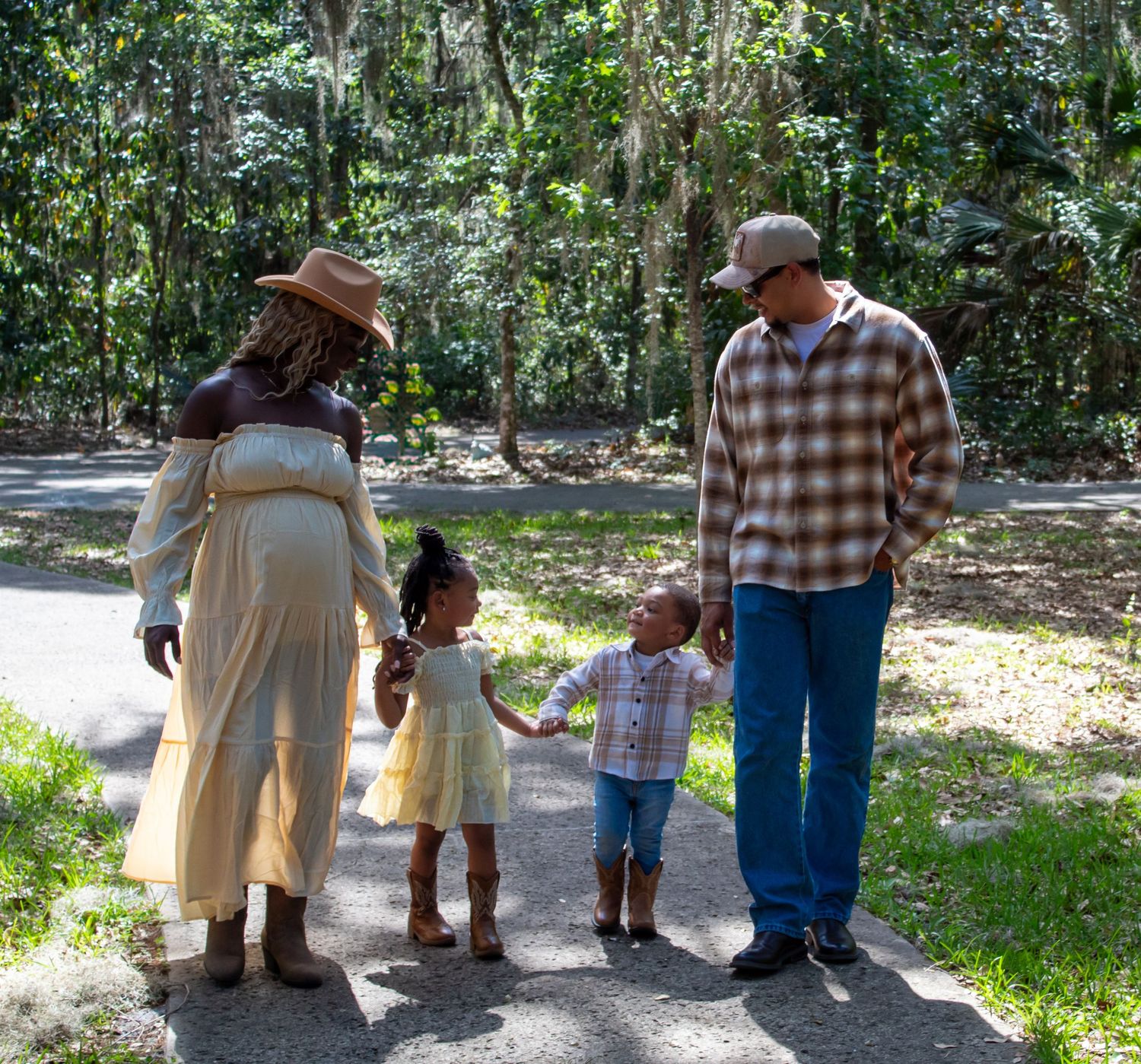 Pregnant Black woman and man walk with two young children on a sunny forest path.