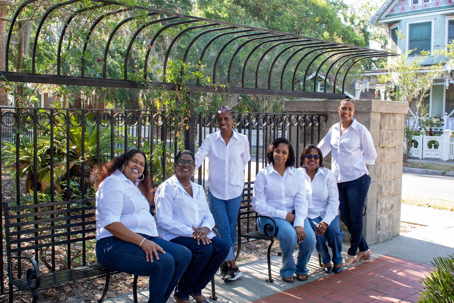 Group of seven people in white shirts and jeans posing near an ornate iron garden gate.