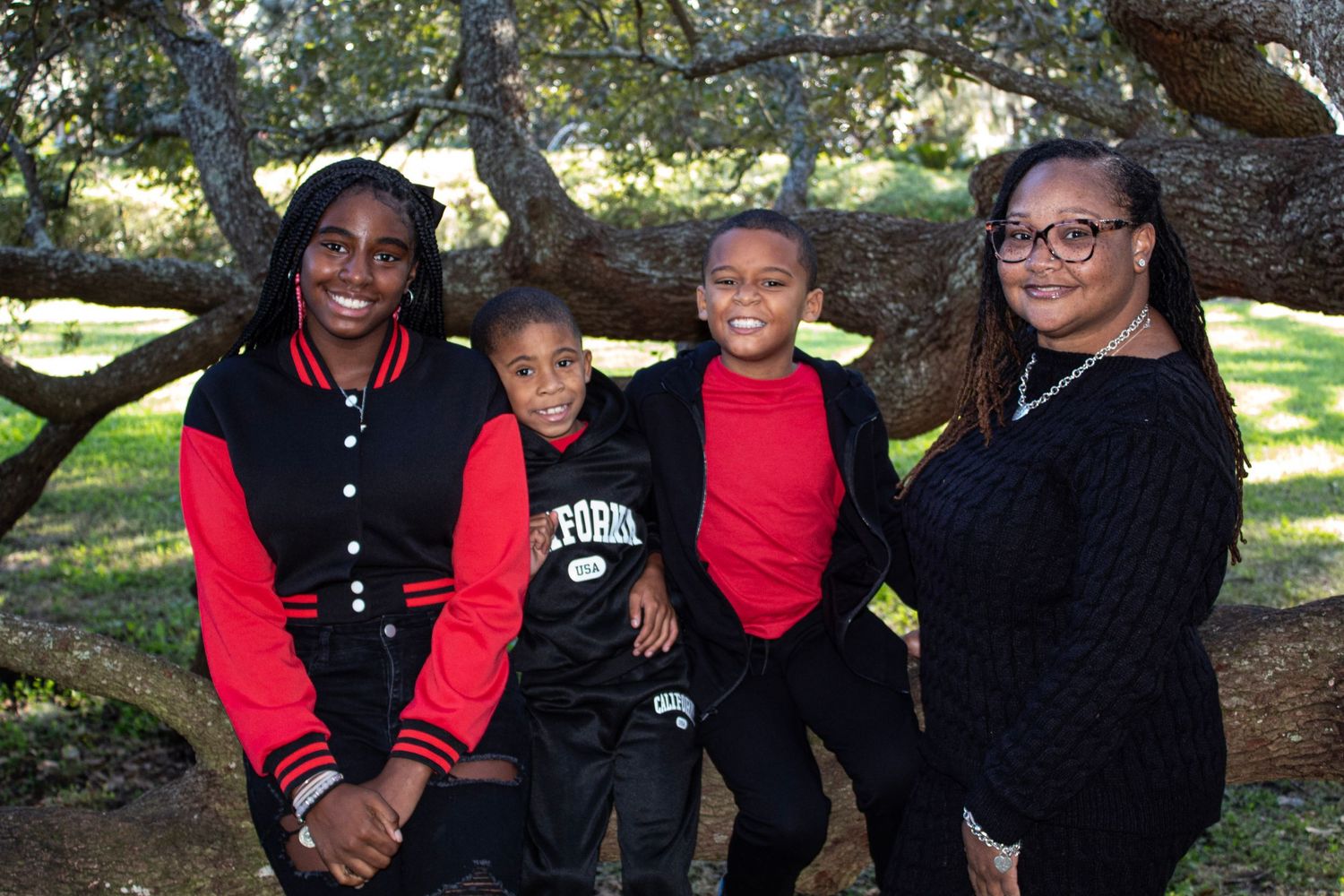Family of four posing outdoors under a tree in coordinating red and black outfits.