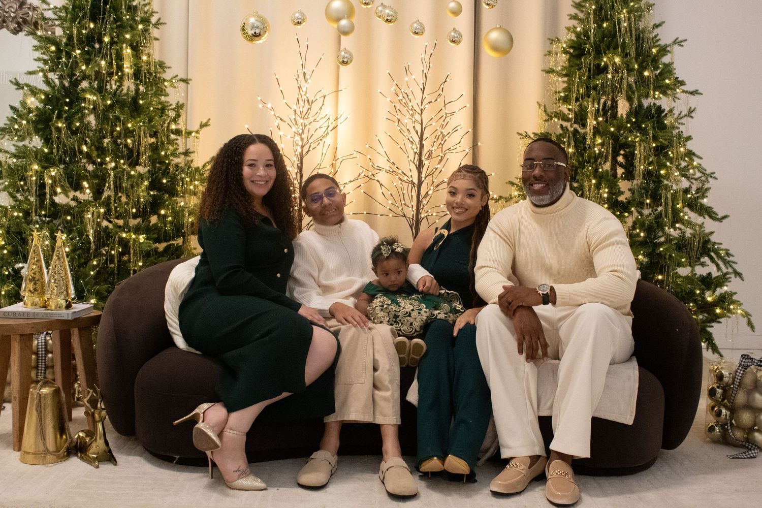 Family of four posing together in front of decorated Christmas trees holiday portrait.