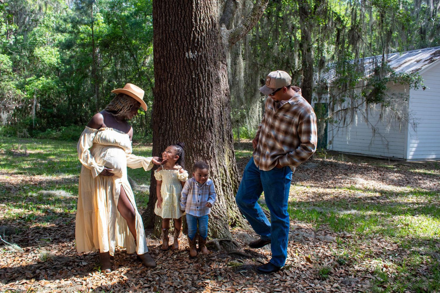 Black family with pregnant mother and children gathered around a tree outdoors.